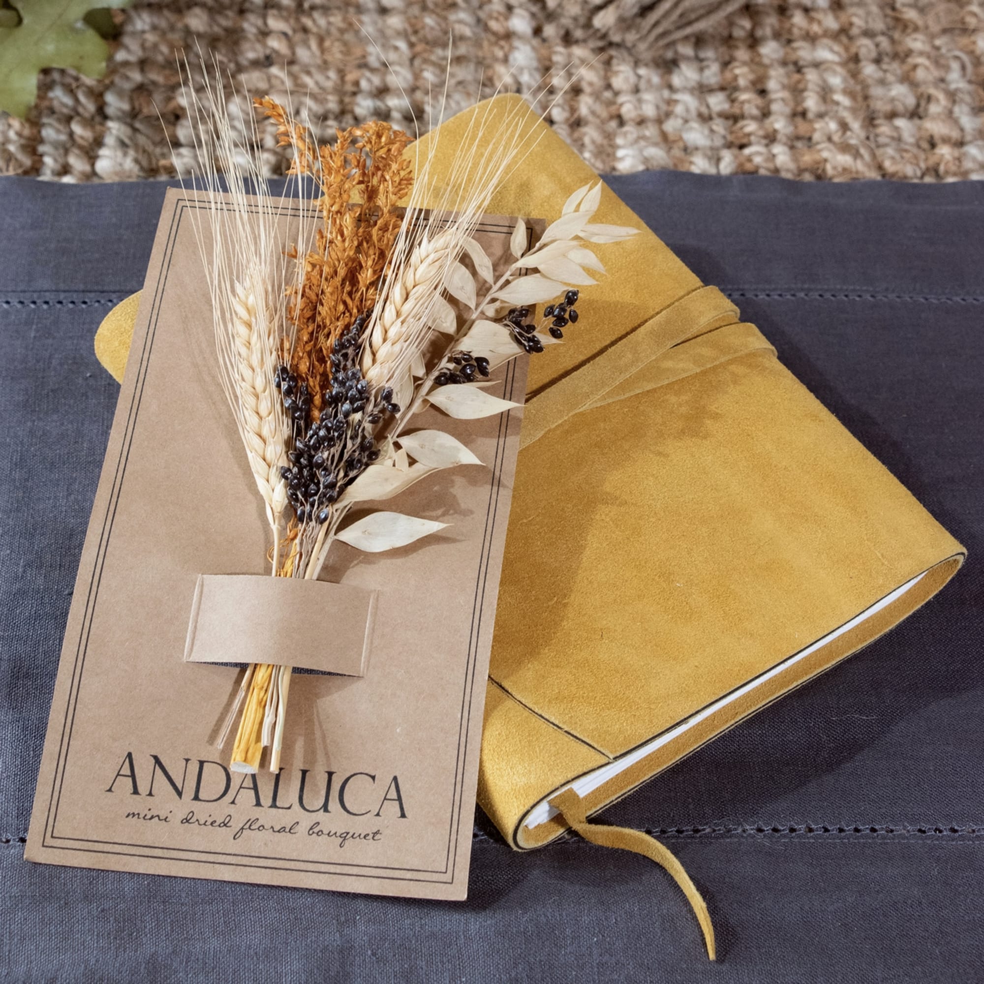 Mini dried floral bouquet in a kraft sleeve beside a mustard notebook