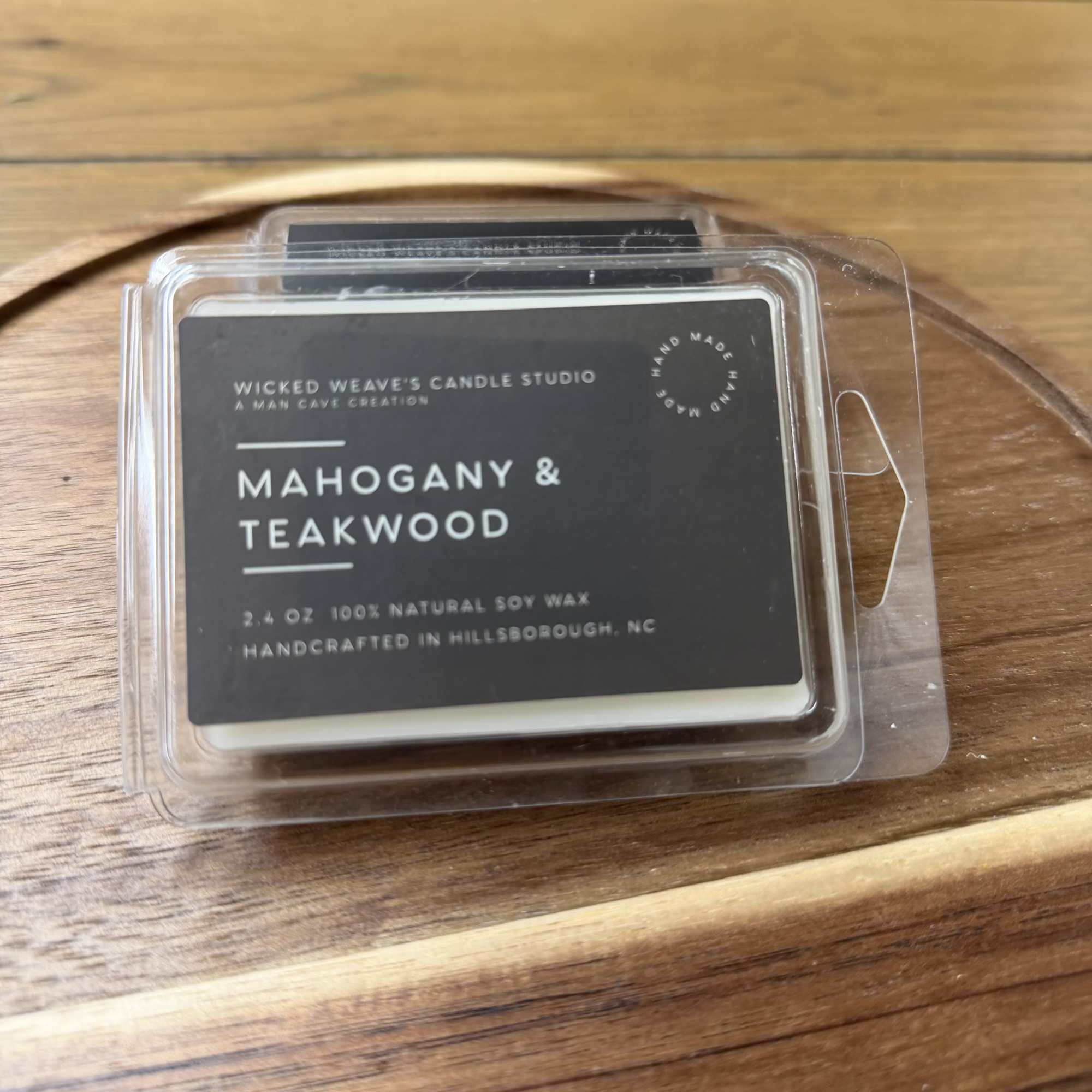 Clamshell candle package labeled Mahogany & Teakwood on a wooden tray