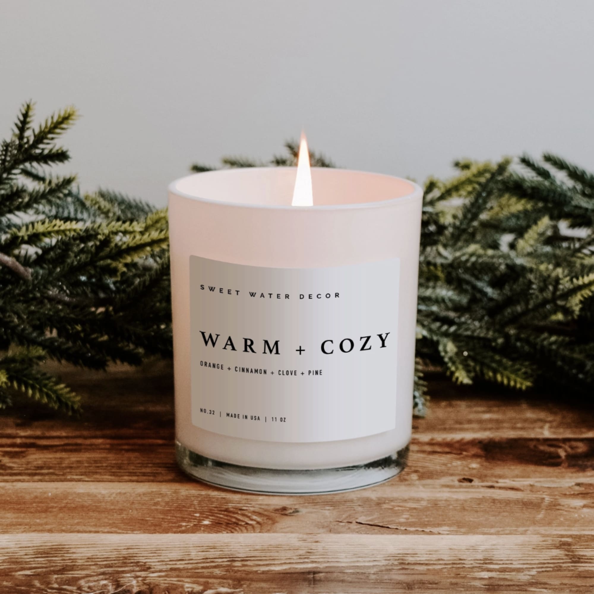 Lit white candle in a glass jar with evergreen branches behind it