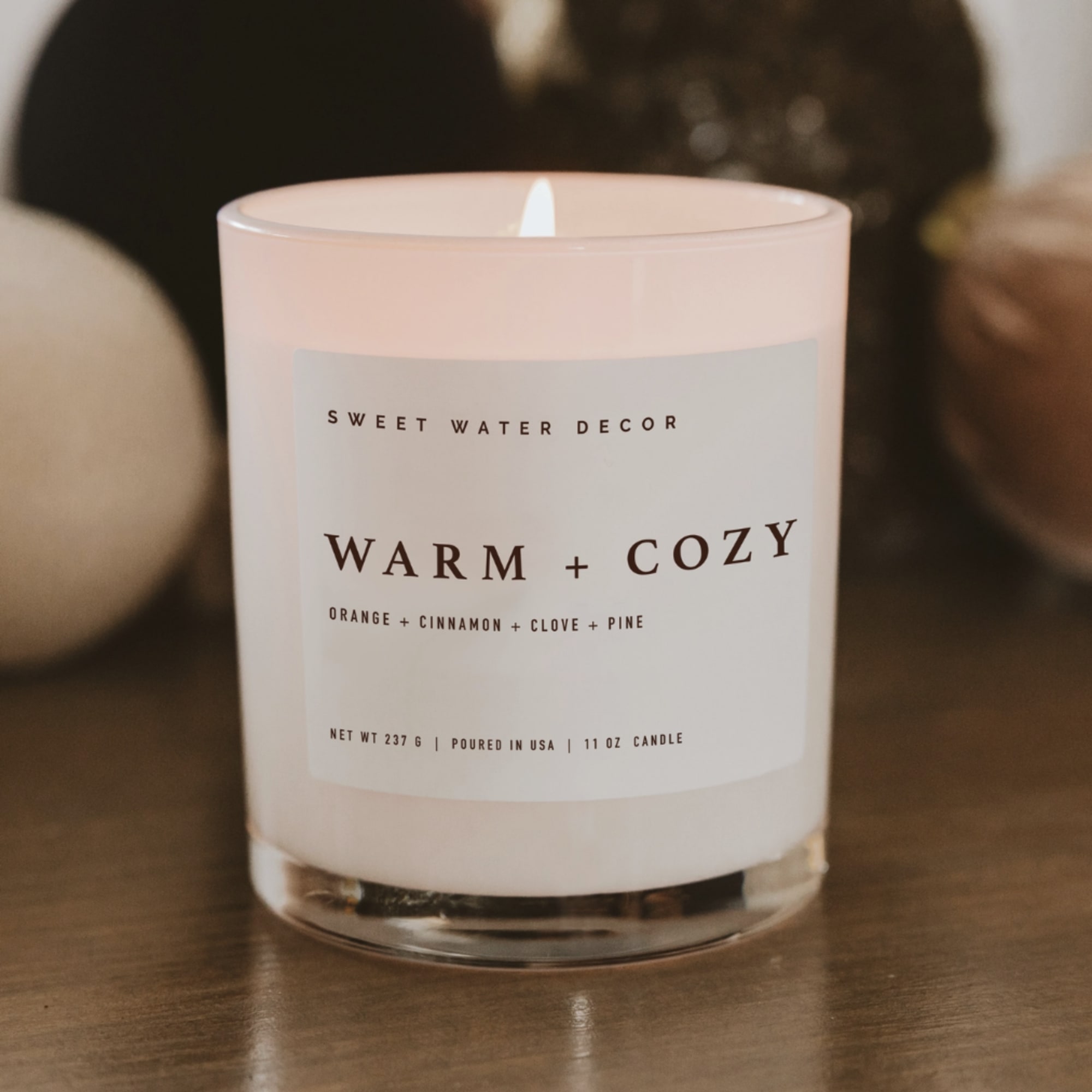 Pink glass candle in a clear tumbler jar with a lit wick