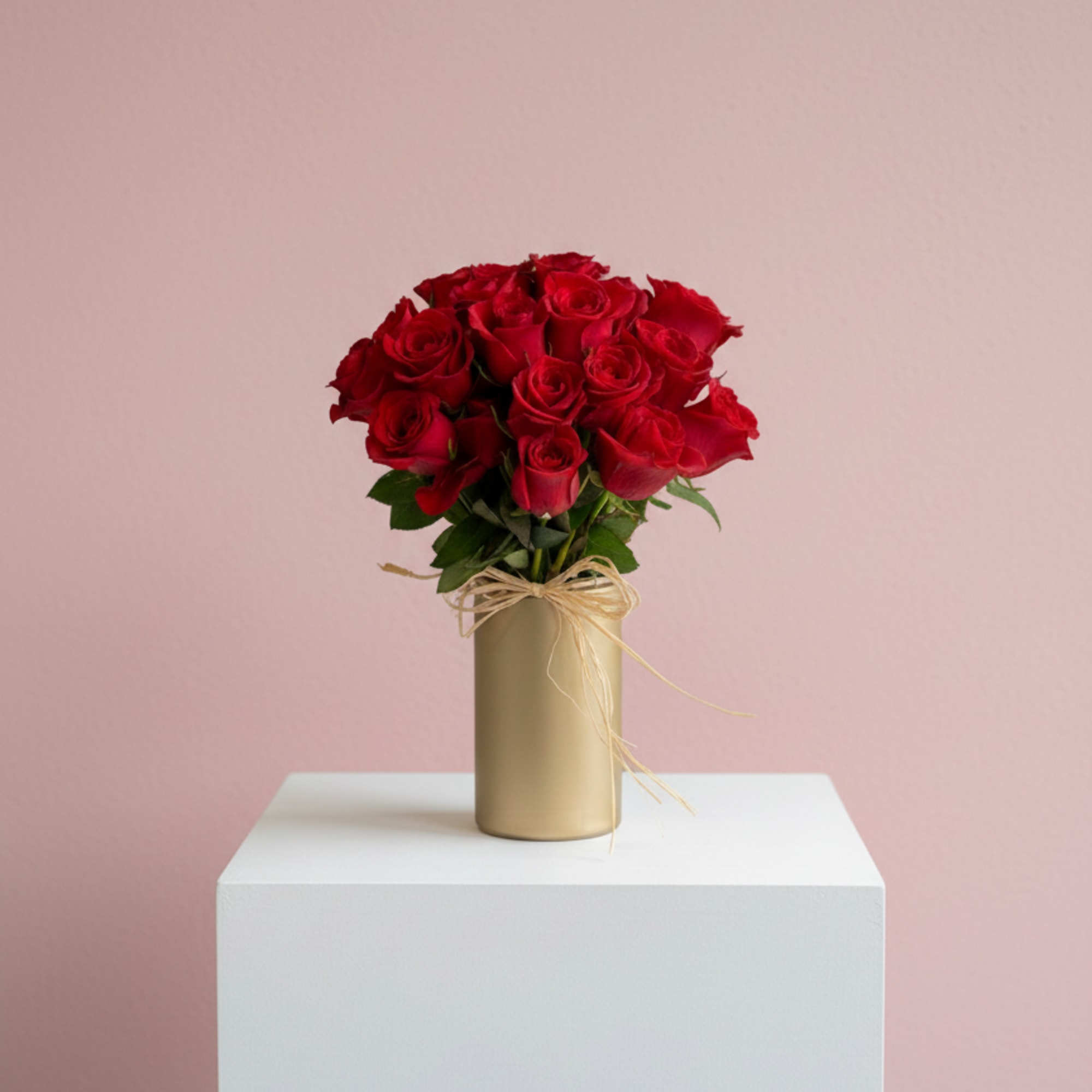 Red roses in a gold vase with a raffia bow