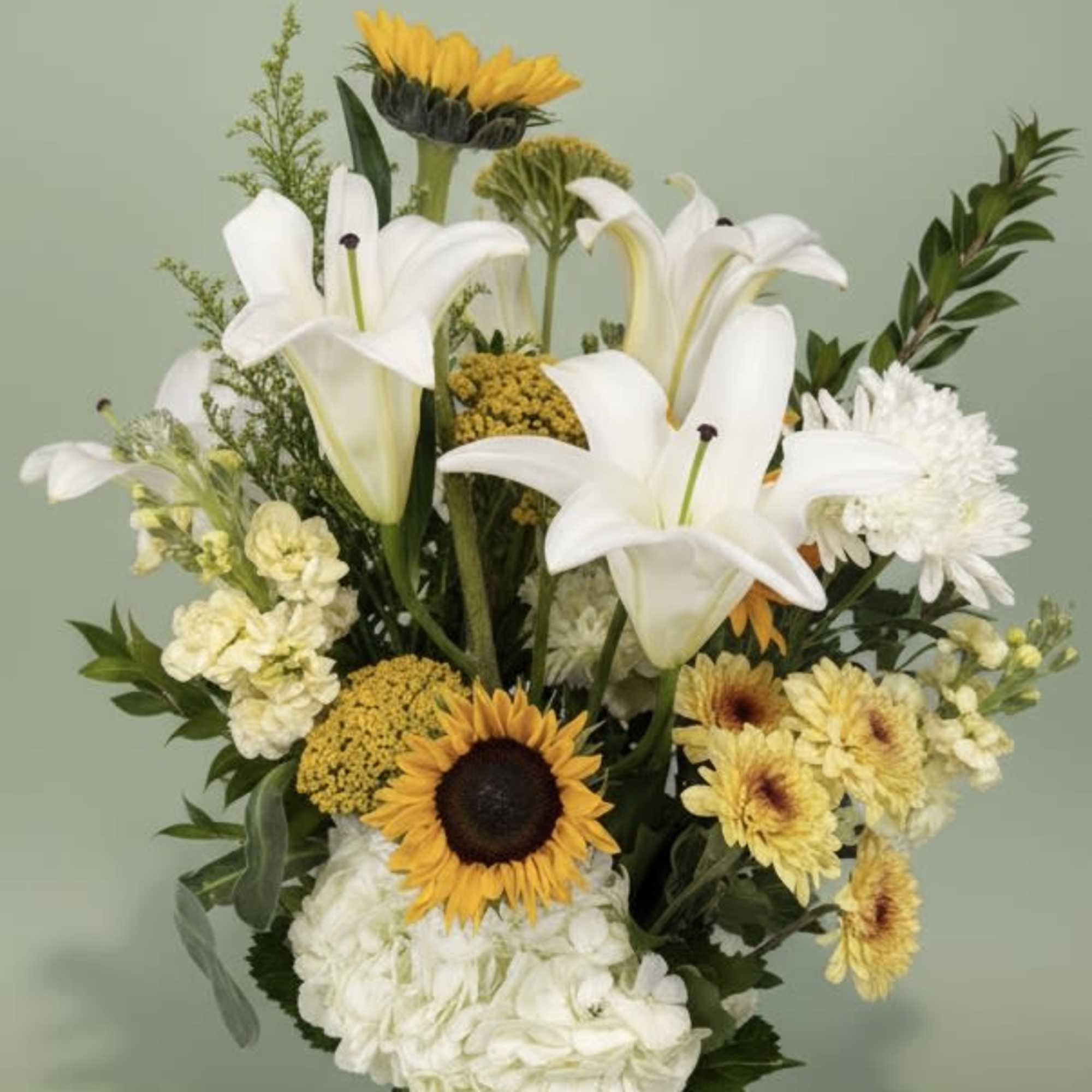 Tall arrangement of white lilies, sunflowers, hydrangeas and yellow mums in a mixed bouquet
