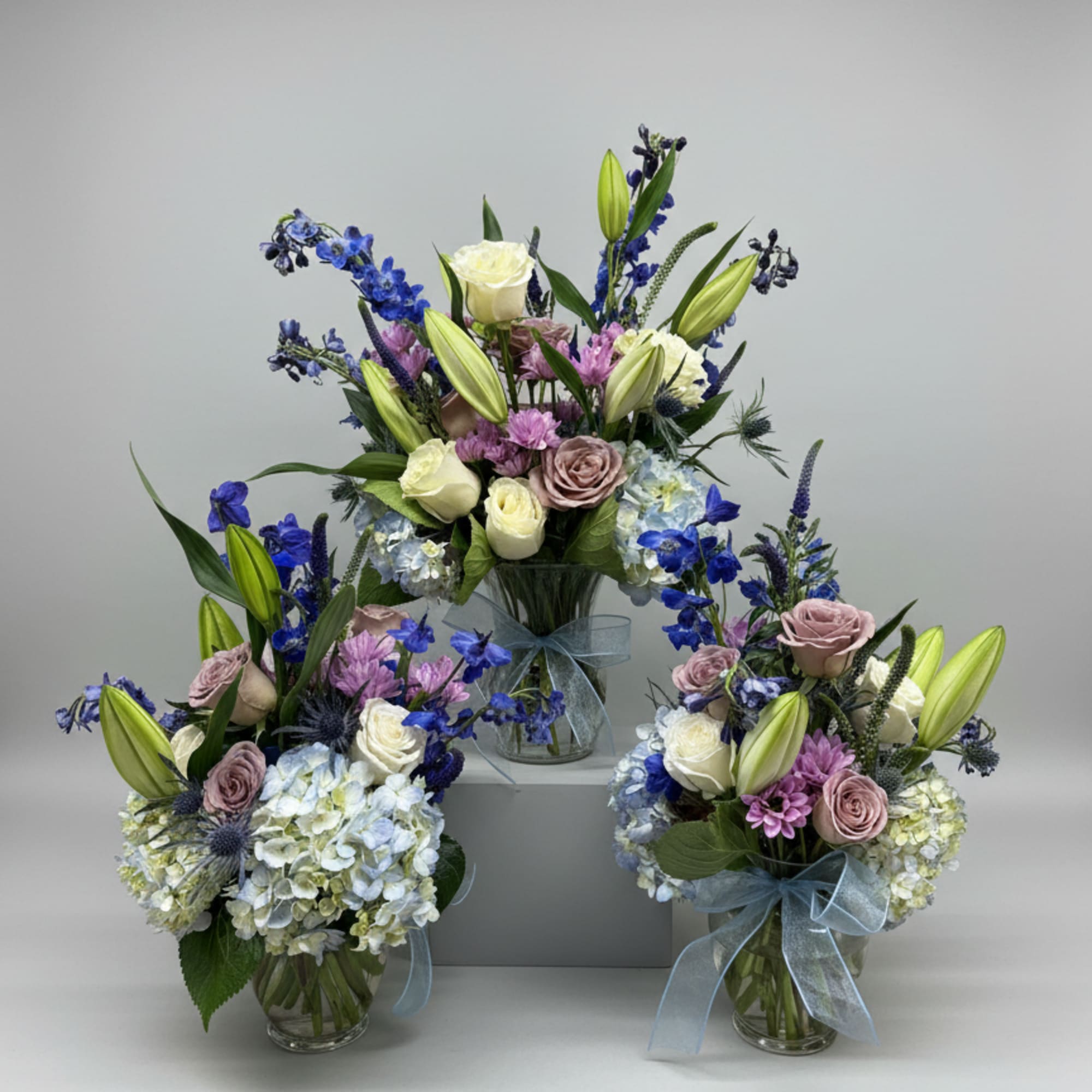 Three pastel floral arrangements in glass vases with blue ribbon bows