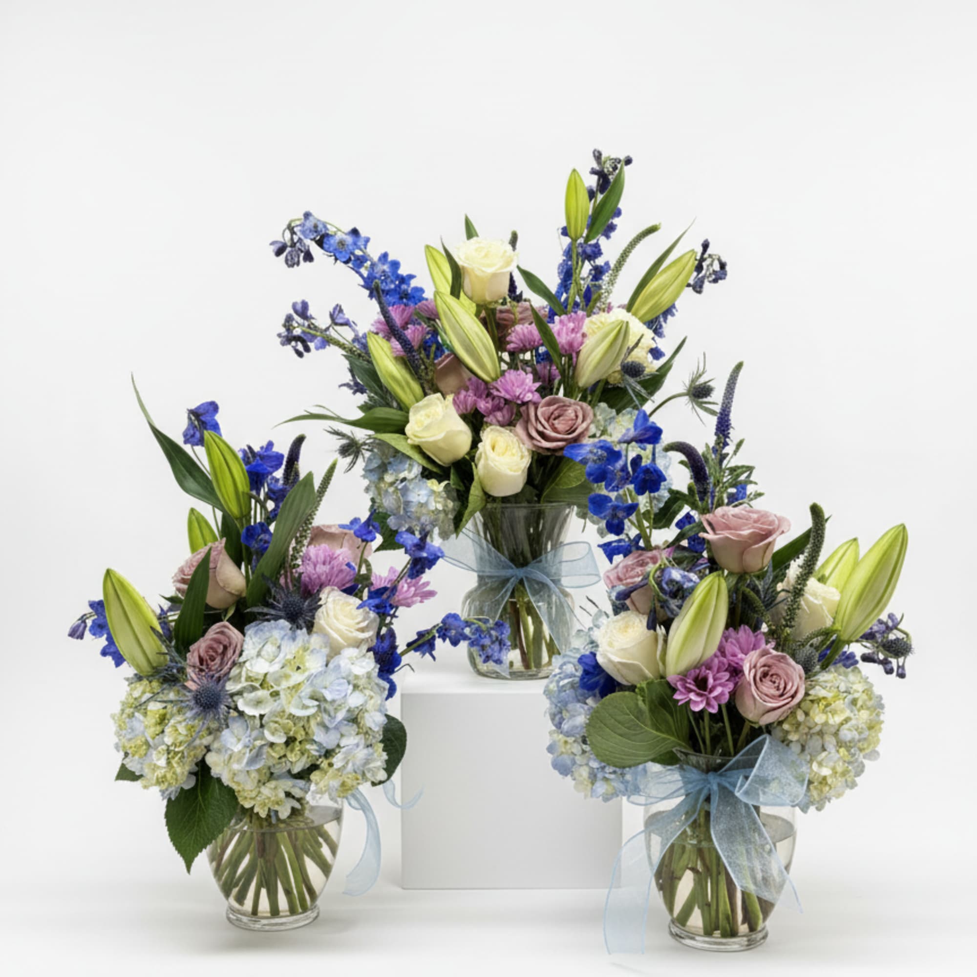 Three mixed flower arrangements in glass vases with blue ribbons