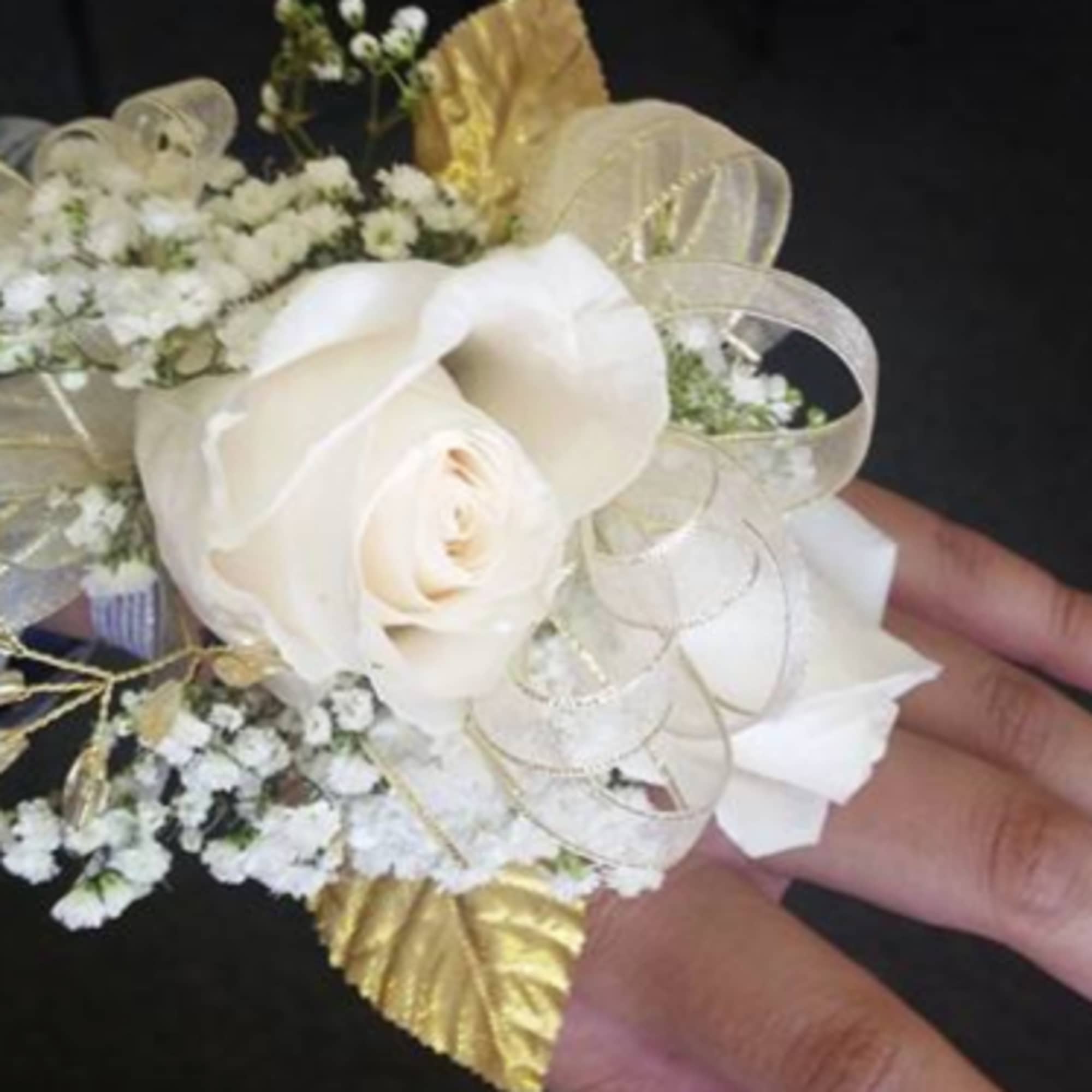 White rose corsage with baby's breath and gold ribbon on a wrist