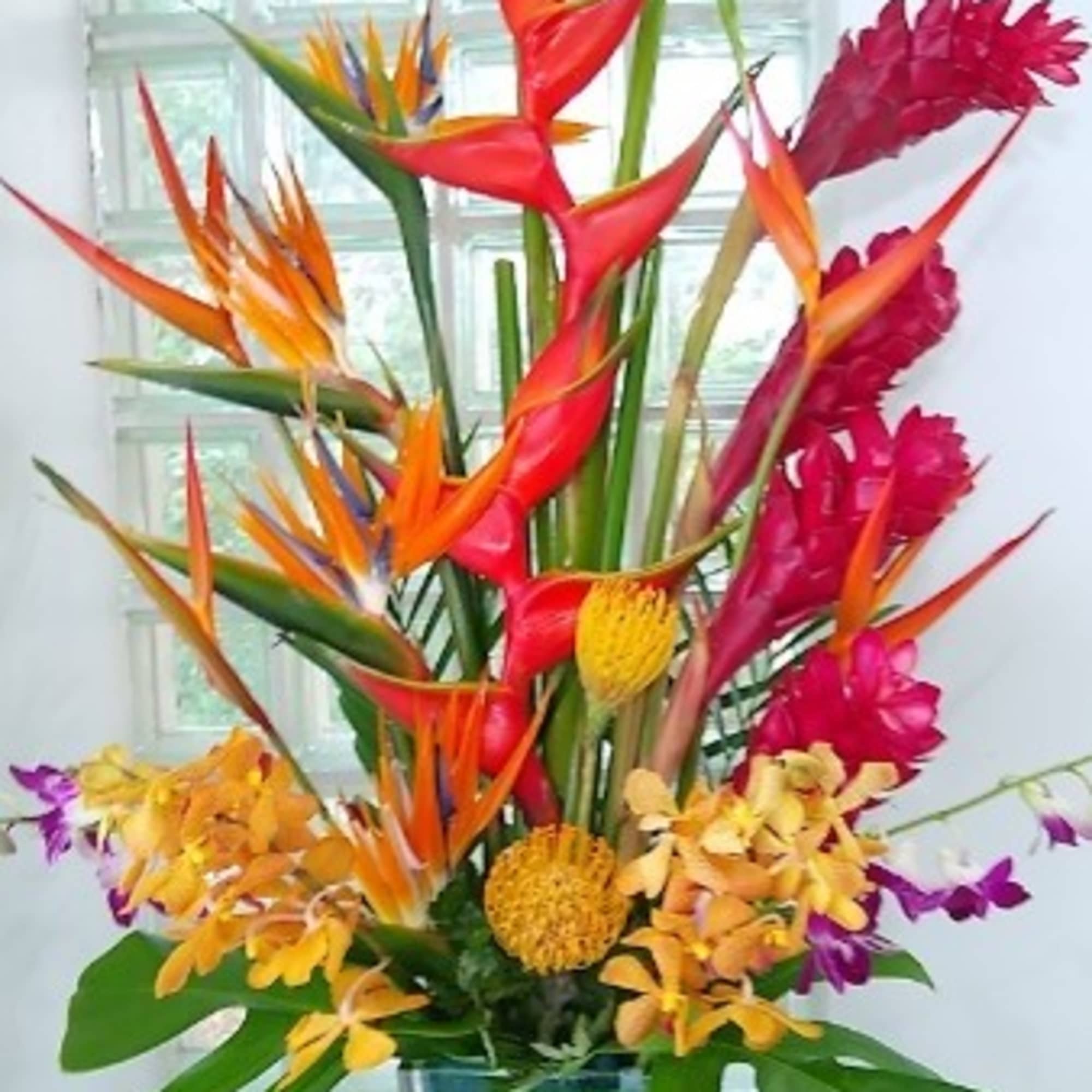 Tall tropical bouquet in a glass vase with orange, red, and yellow blooms