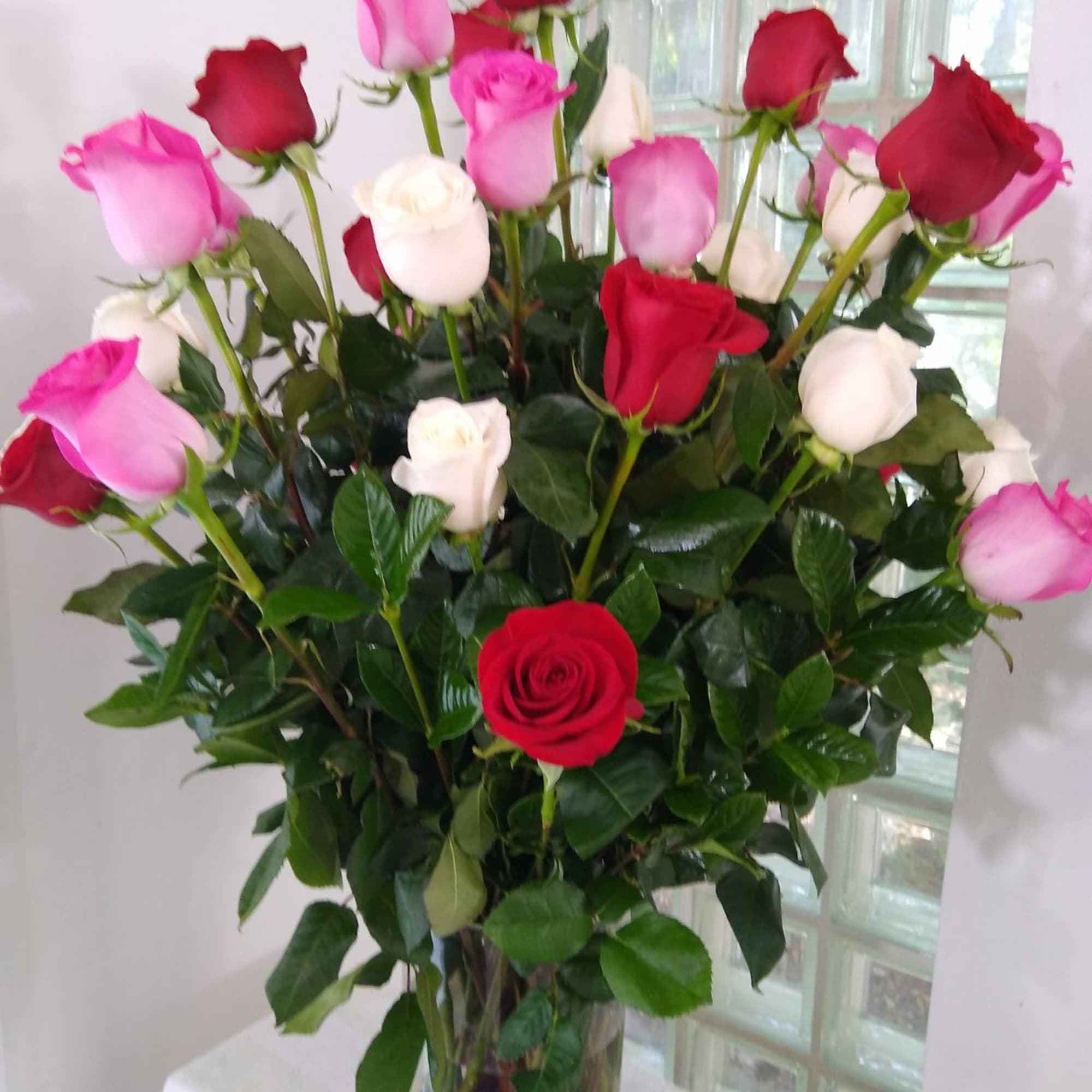 Tall arrangement of red, pink, and white roses in a clear glass vase