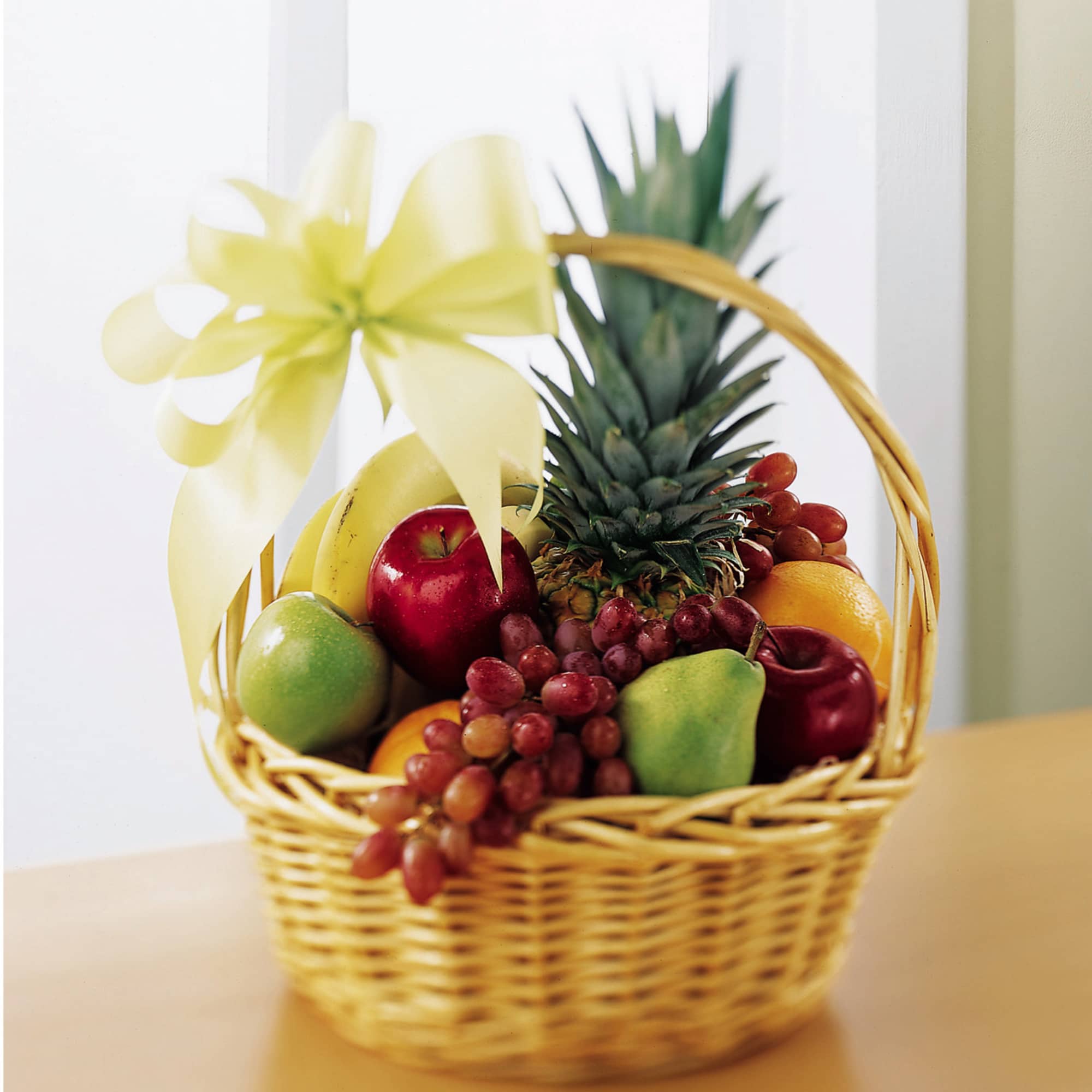 Wicker gift basket filled with assorted fresh fruits and topped with a large yellow bow