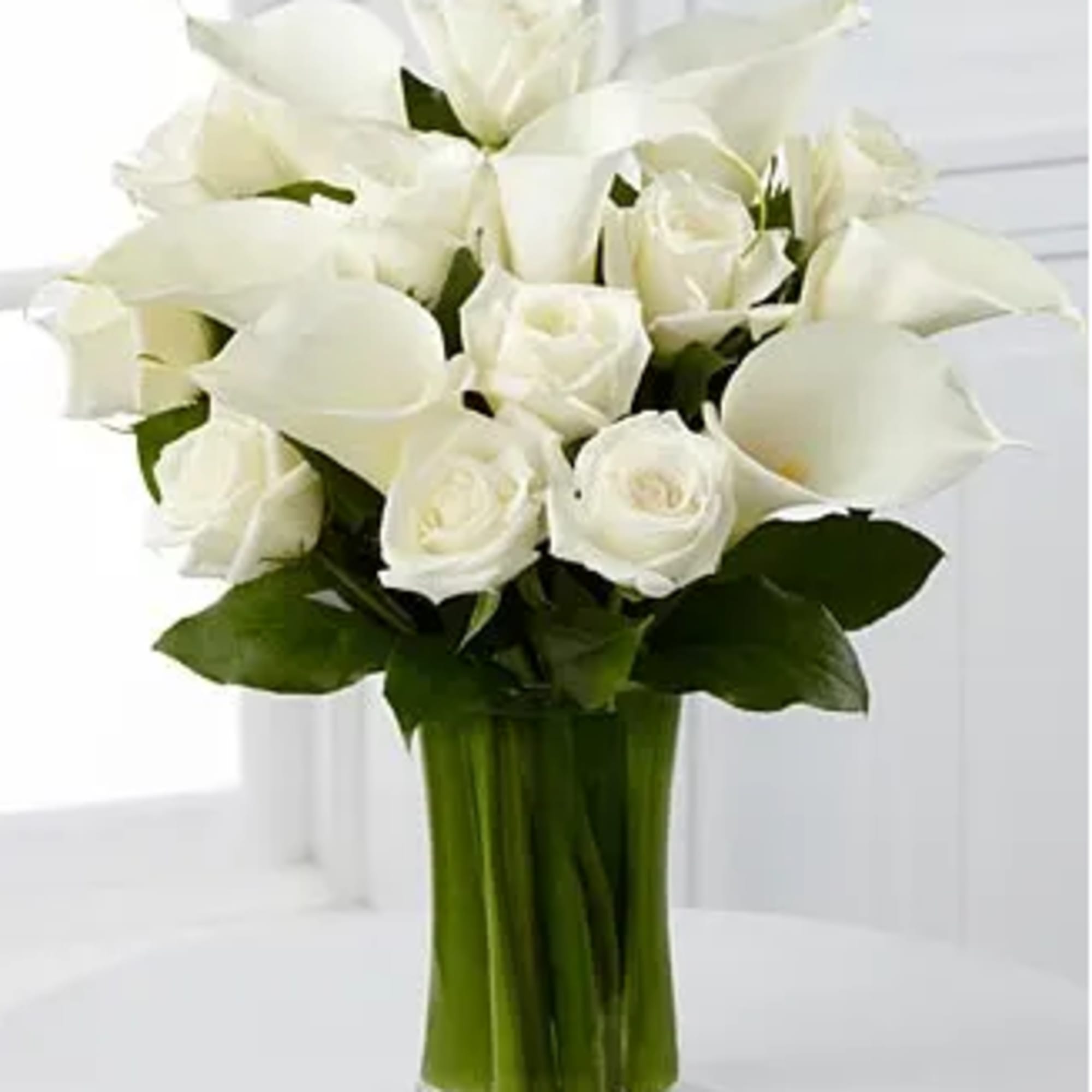 White calla lilies and roses arranged in a clear glass vase