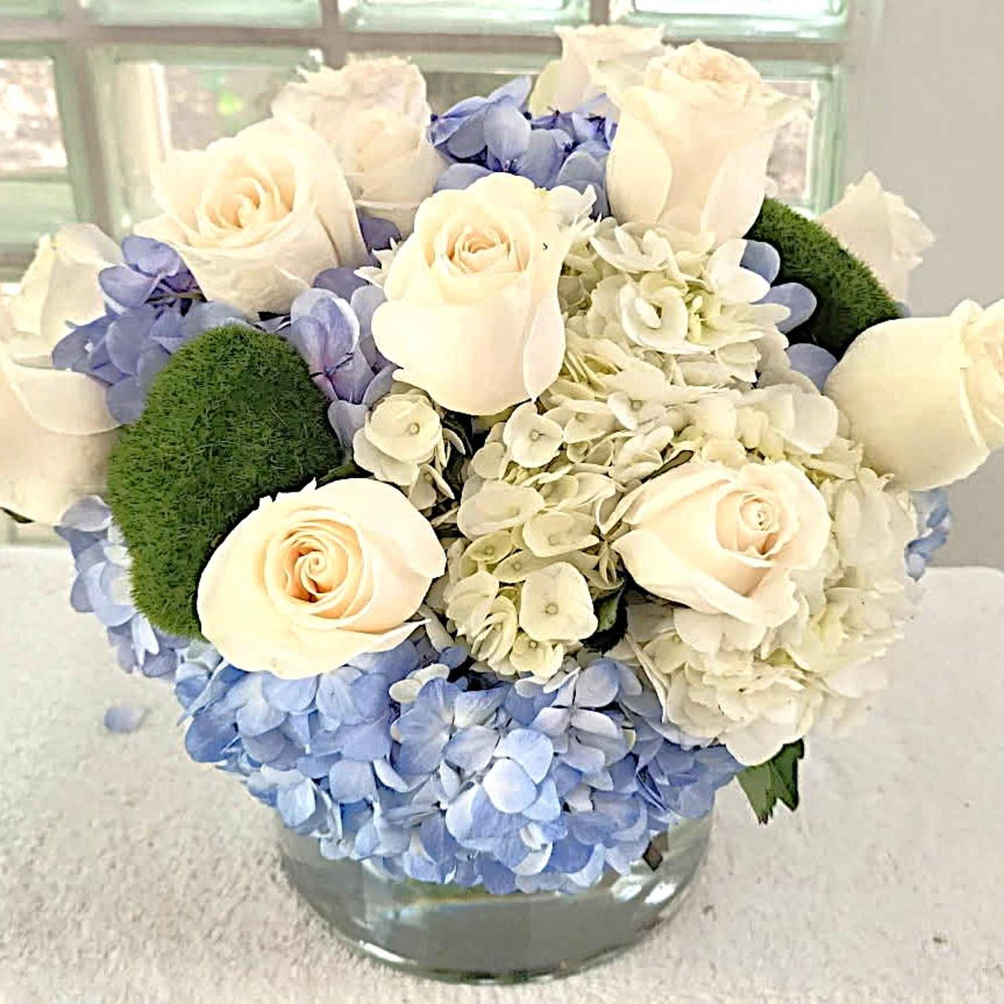 Creamy white roses gathered with pale green and soft blue hydrangeas create