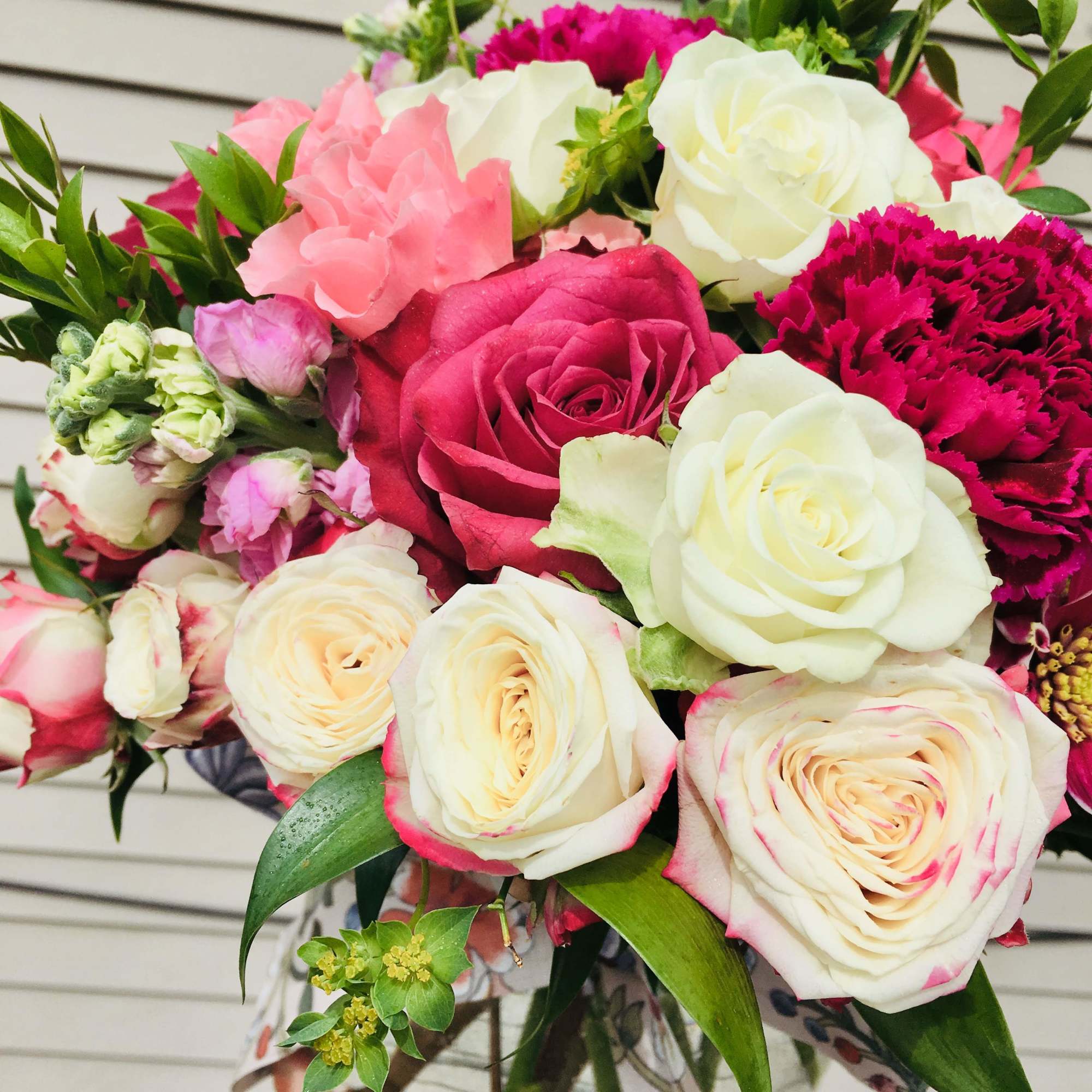 Mixed bouquet of white and pink roses with bright fuchsia blooms in a clear glass vase.