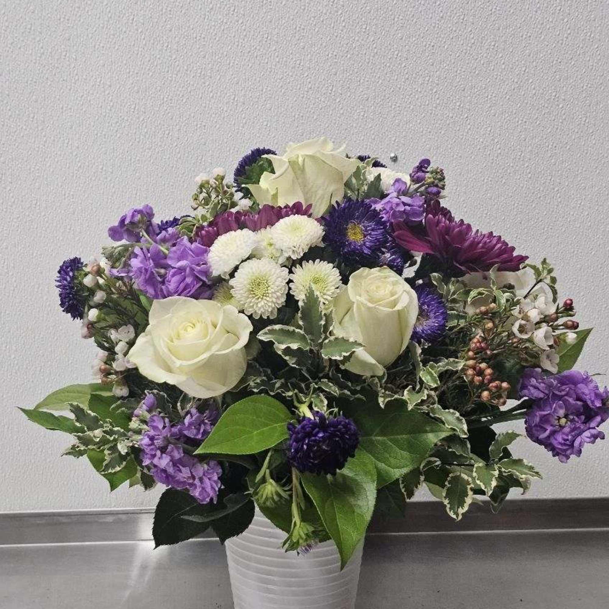 White roses and purple mixed flowers arranged in a white ceramic vase