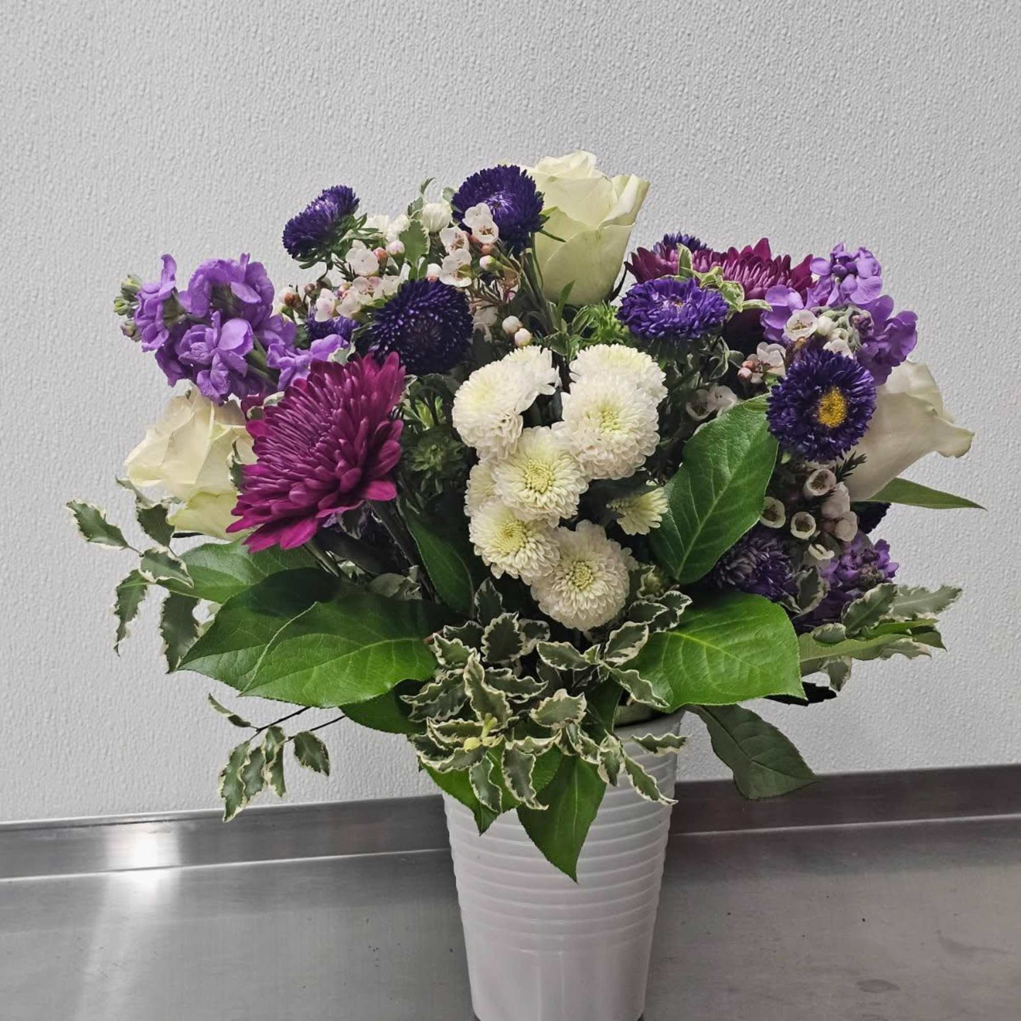 Purple and white mixed flower arrangement with roses and mums in a white vase