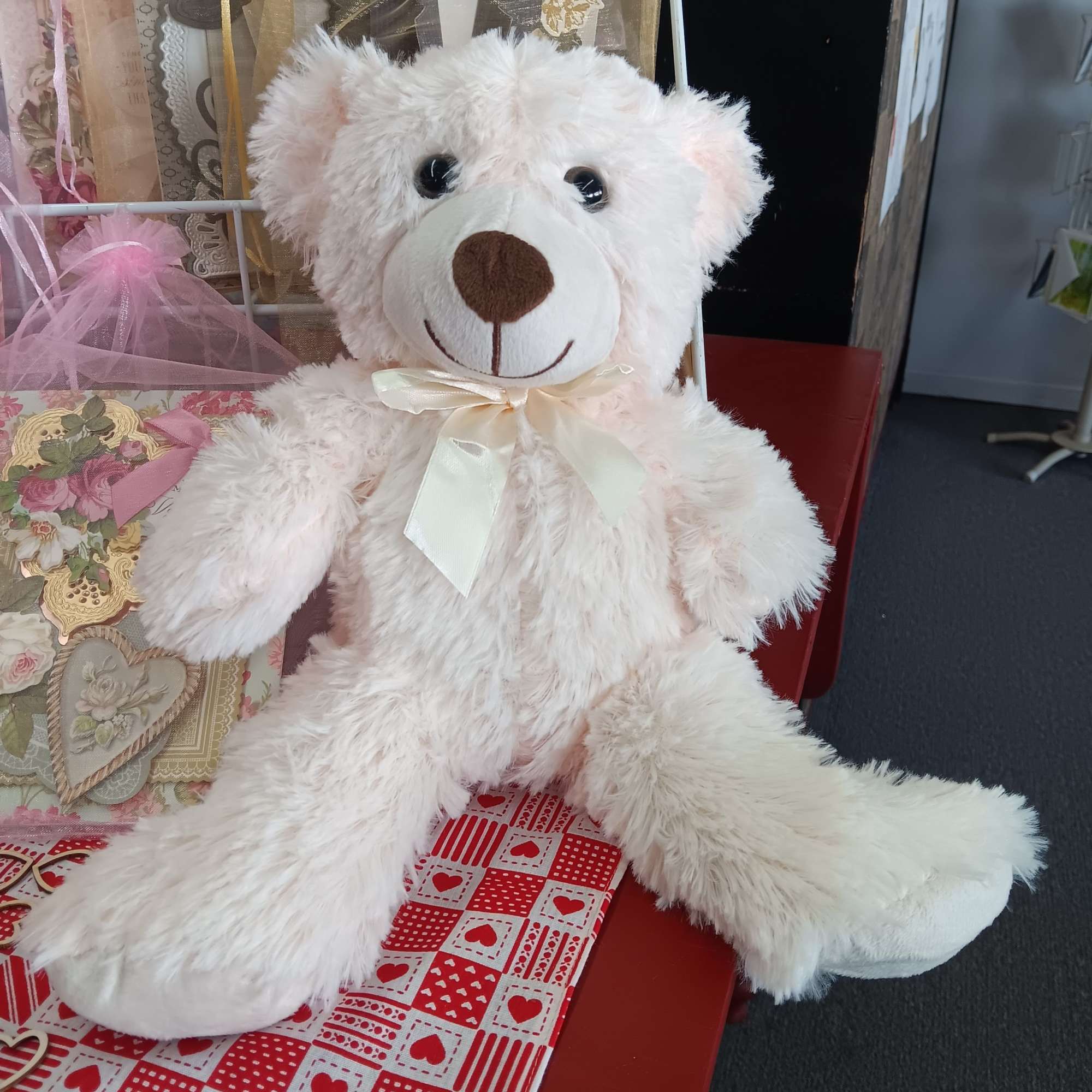 White teddy bear with a satin bow sitting among gift cards