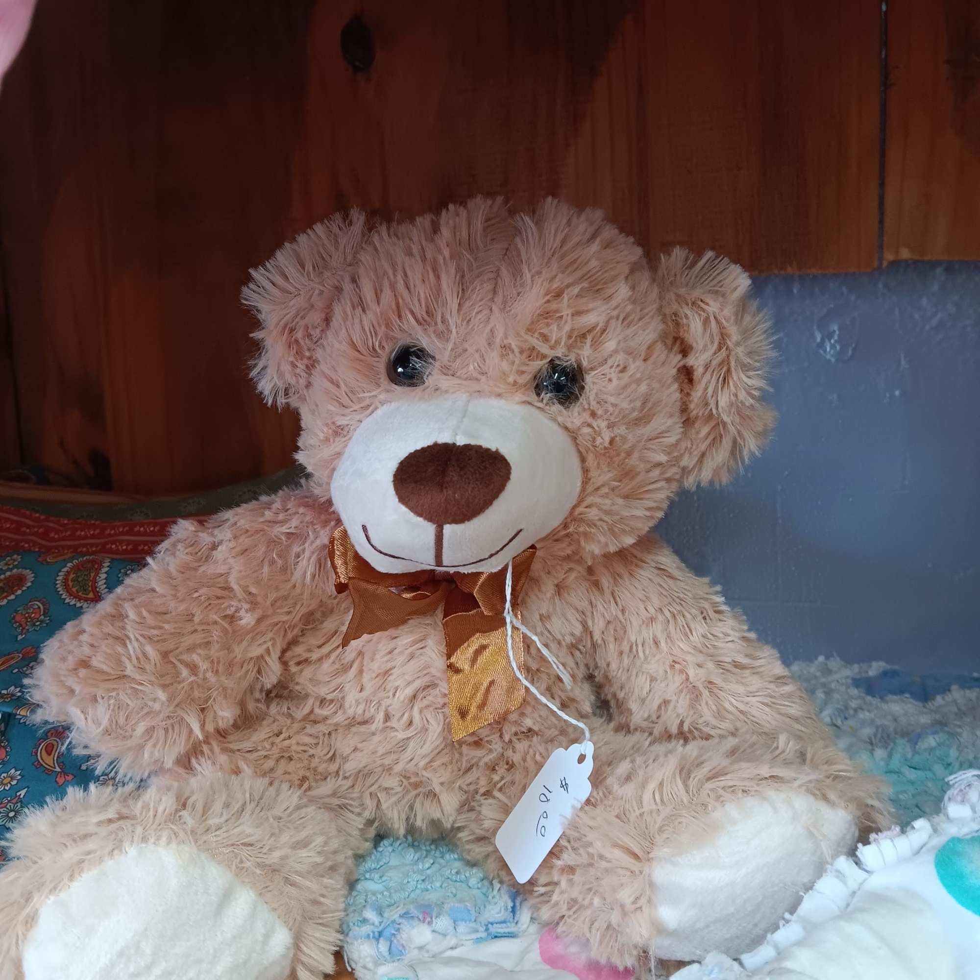 Large plush teddy bear with a ribbon bow sitting on a bed