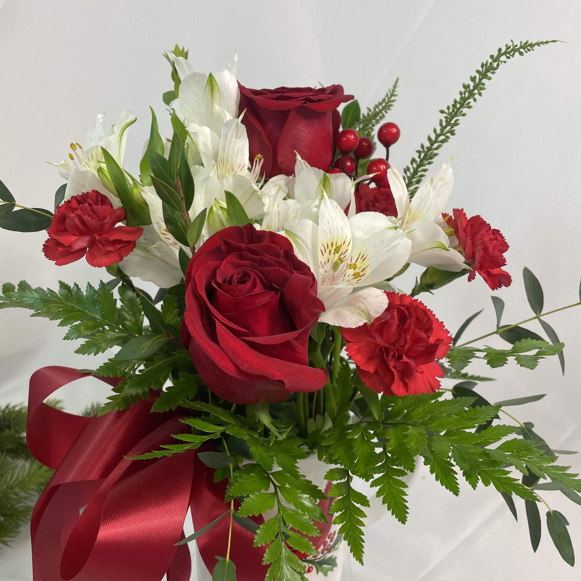 Red roses and white alstroemeria in a vase with a red ribbon