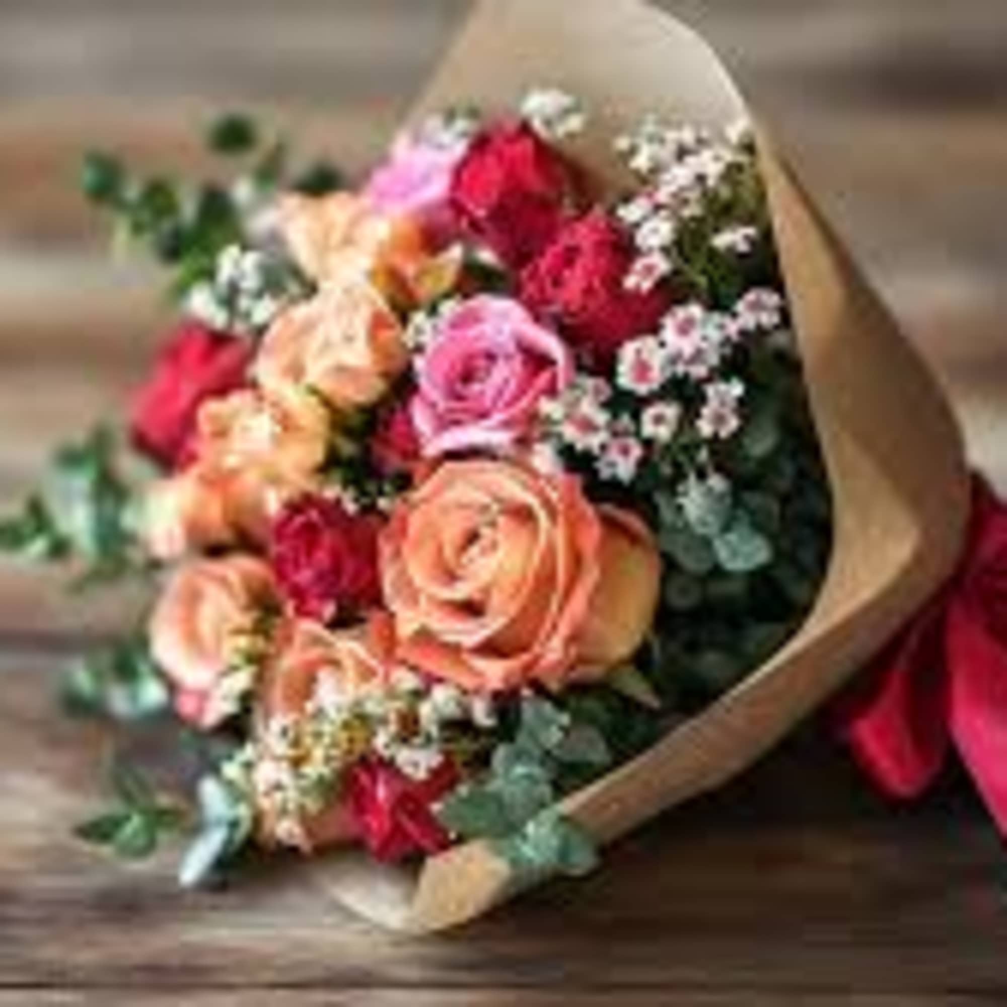 Bouquet of pink, peach, and red roses wrapped in brown paper with a red ribbon