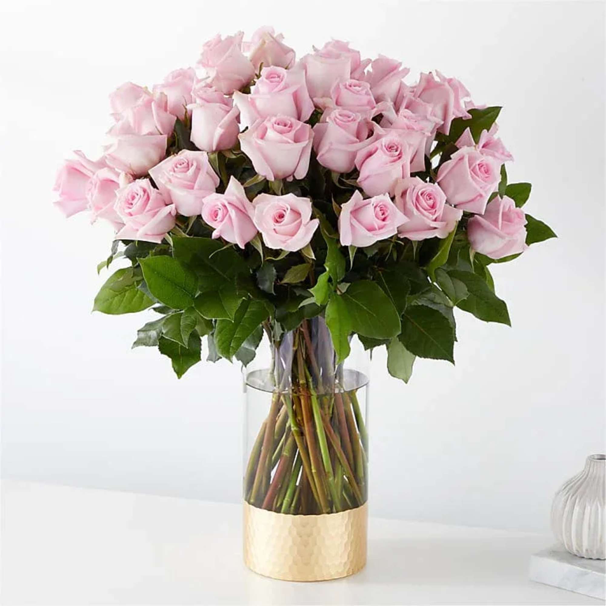 Pink roses arranged in a clear glass vase with a gold base