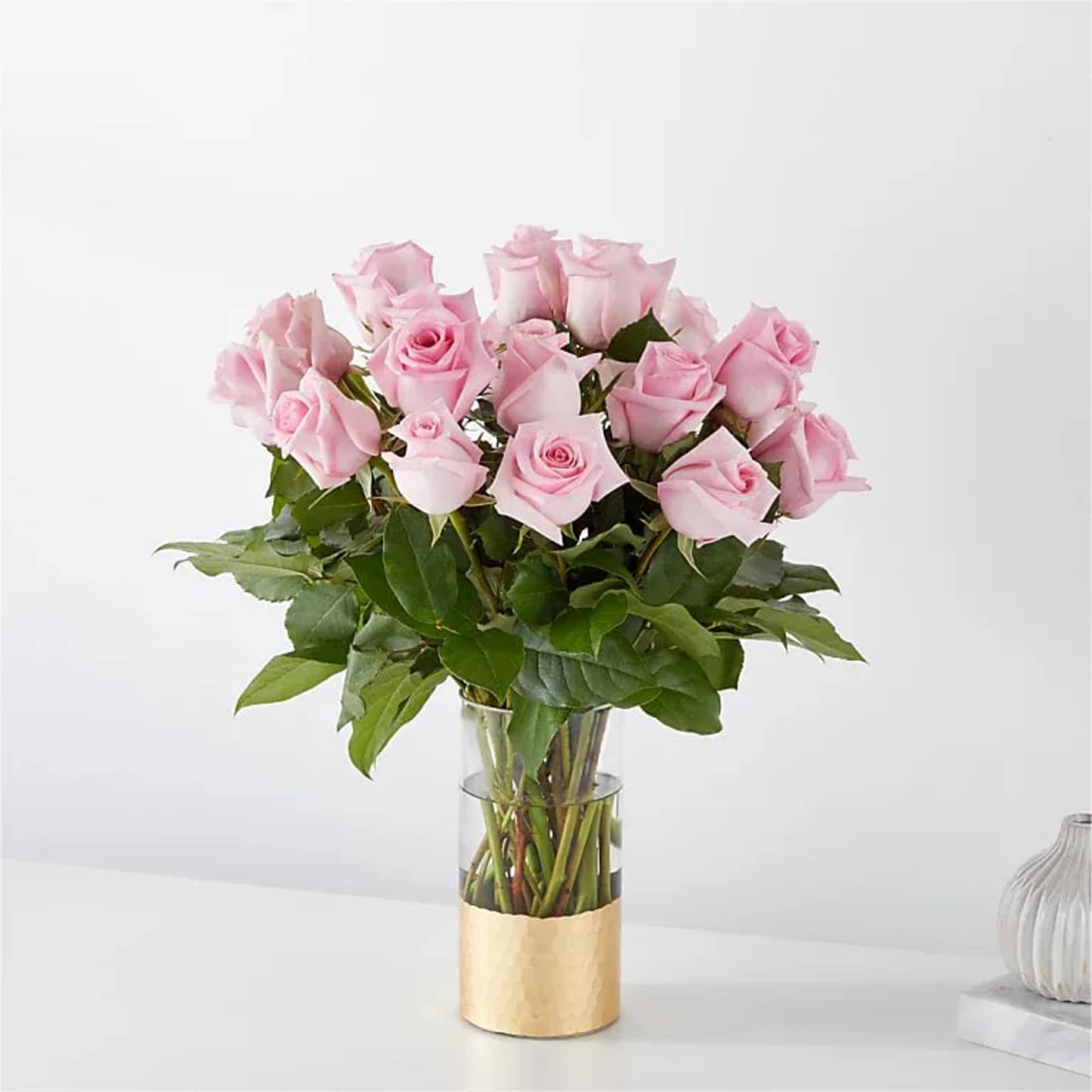 Pink roses arranged in a clear glass vase with a gold wrap