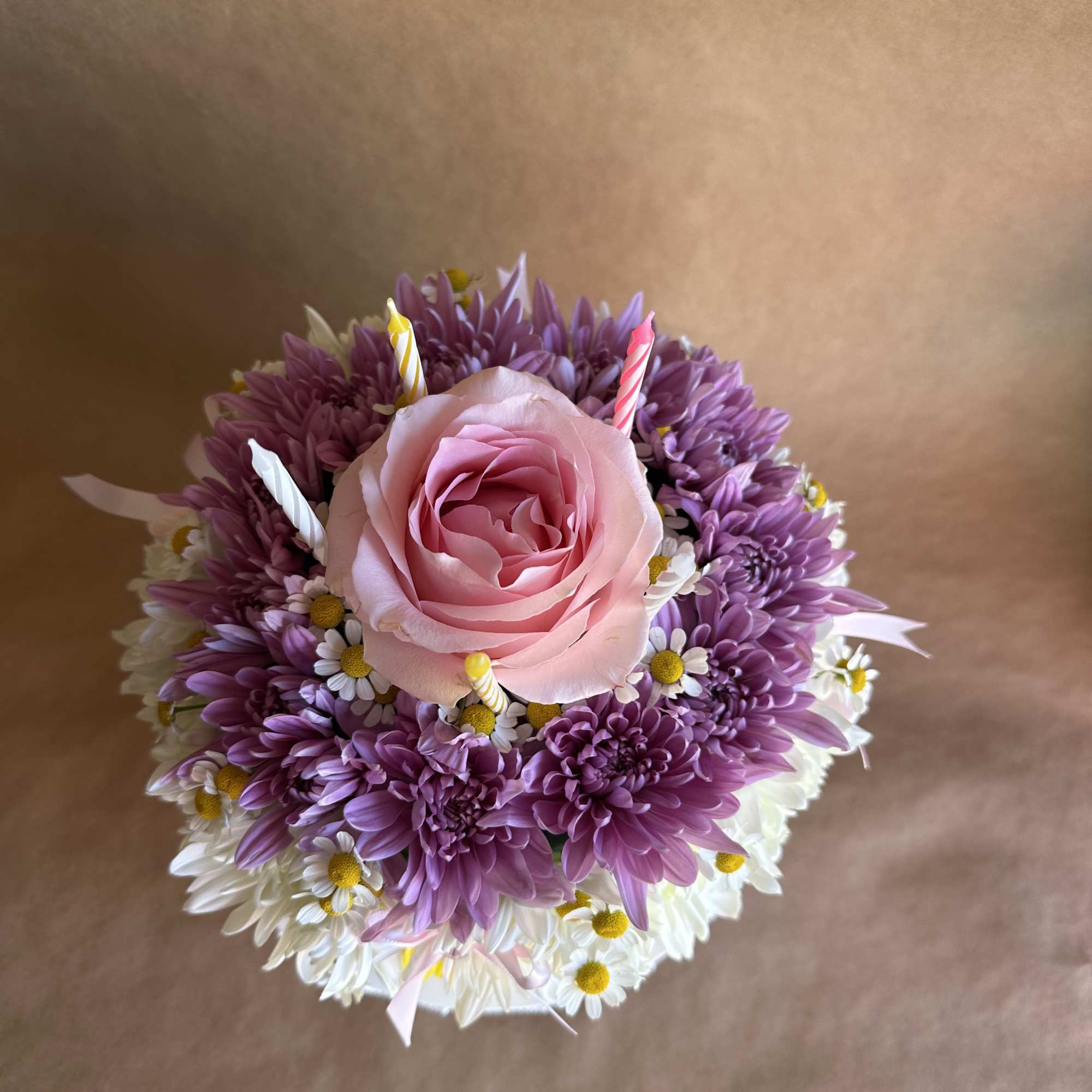 Pink rose surrounded by purple and white daisies with small candles