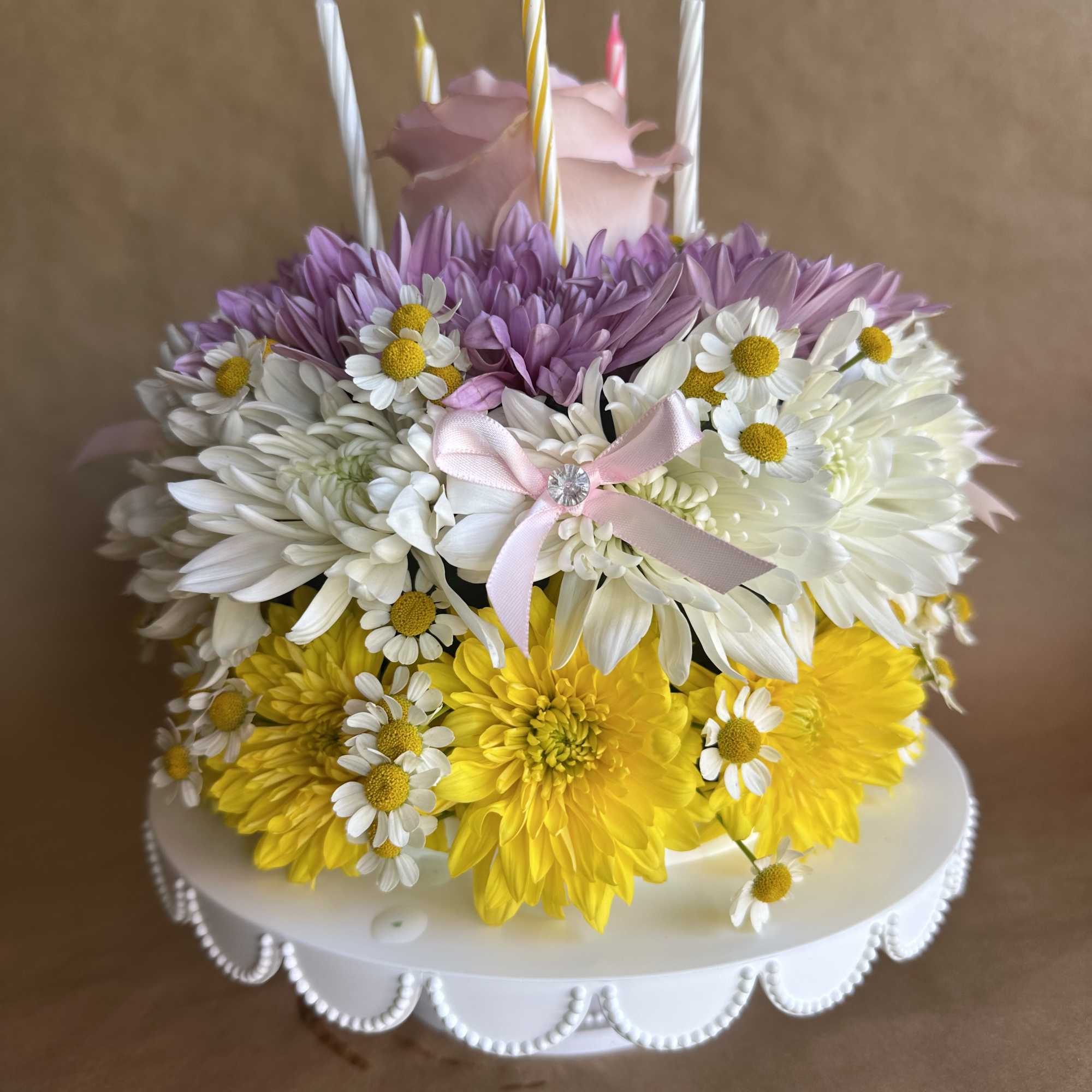 Flower-covered cake with candles and a pink rose topper