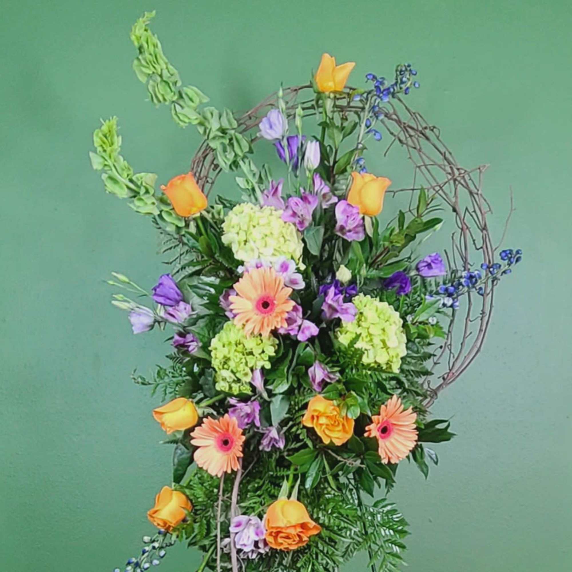 Tall floral arrangement with orange and purple blooms in a twig hoop frame