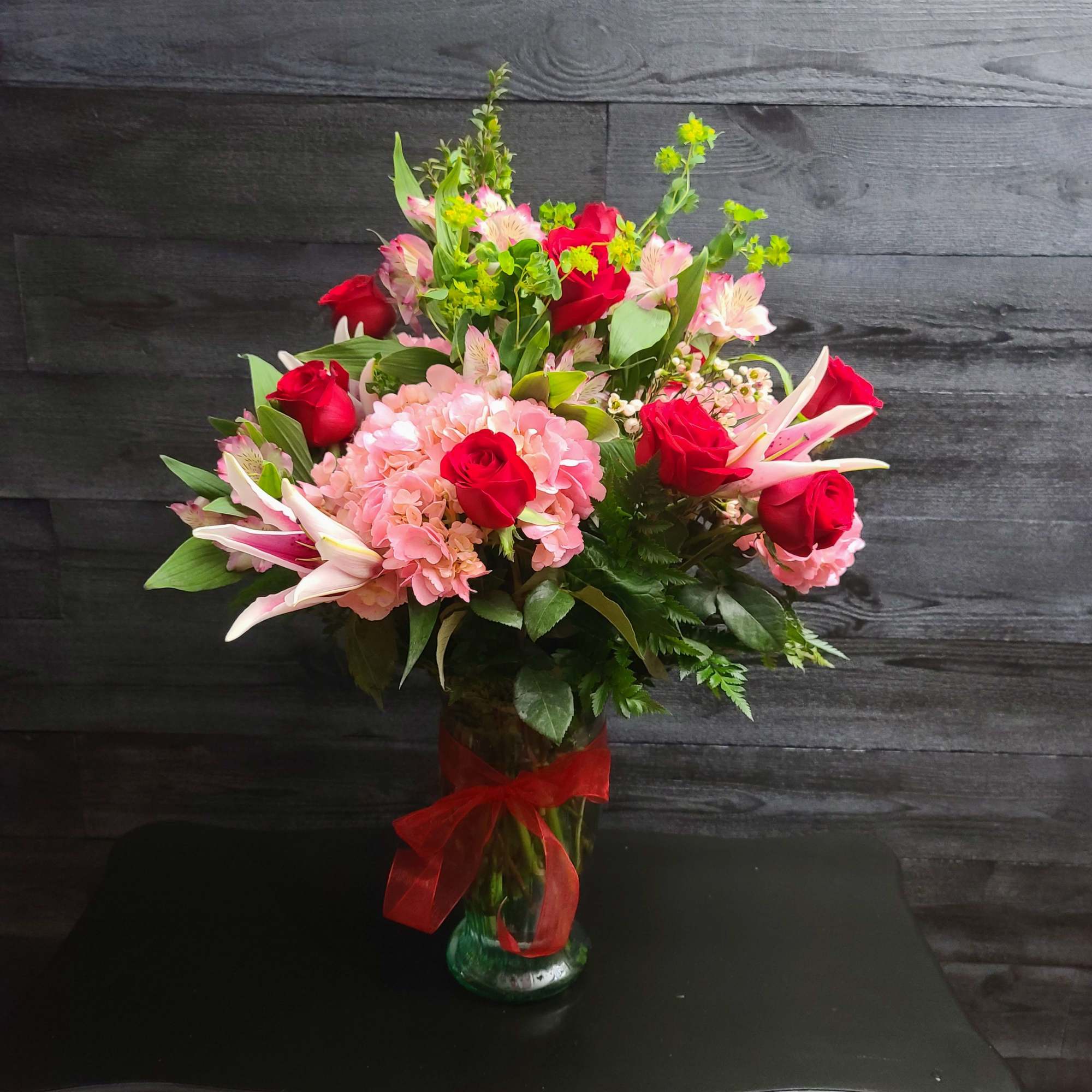 Bouquet of red roses, pink hydrangeas, and lilies in a glass vase