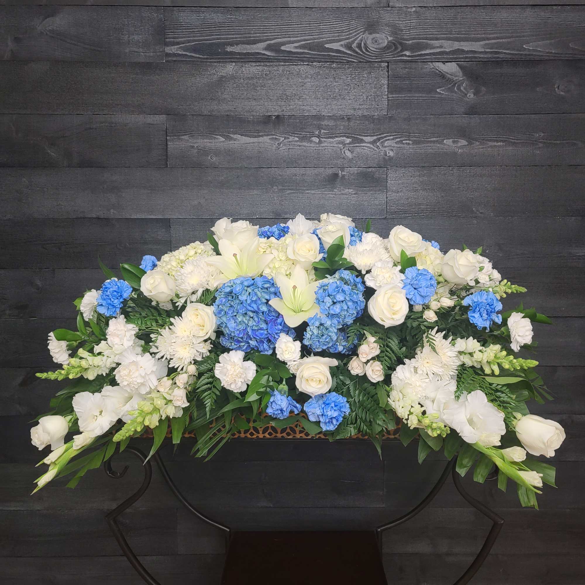 Casket Spray only. Blue delphinium, white lilies and other seasonal blooms. Approximately