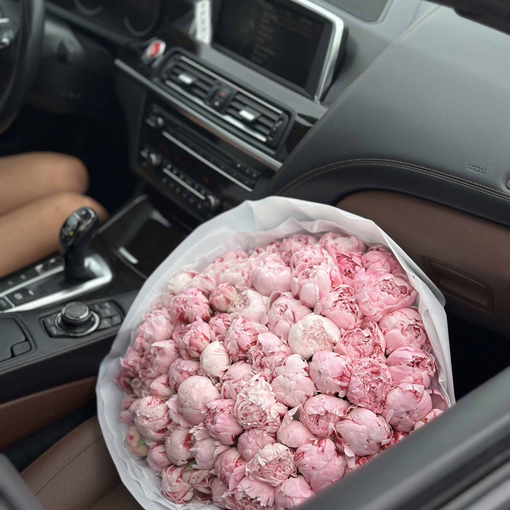 Large bouquet of pink peonies wrapped in white paper on a car seat, photo 3 of 3