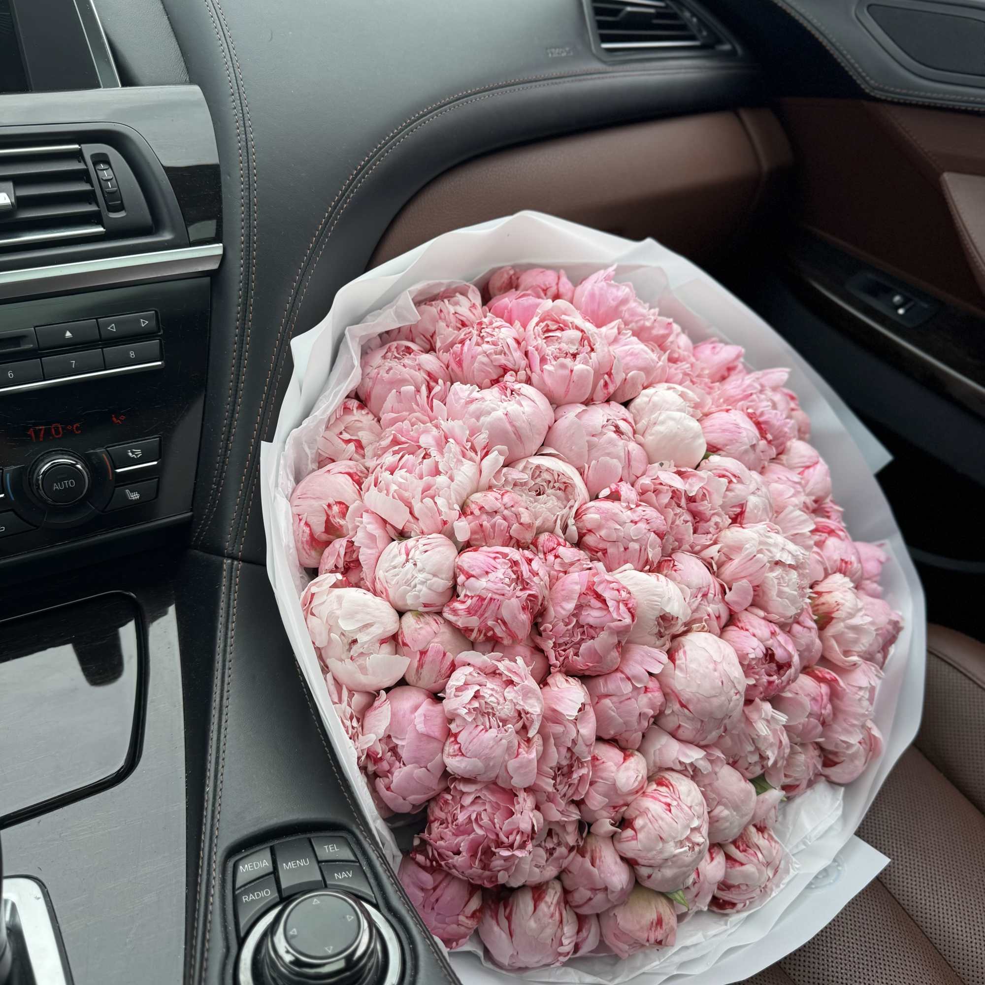 Large bouquet of pink peonies wrapped in white paper on a car seat
