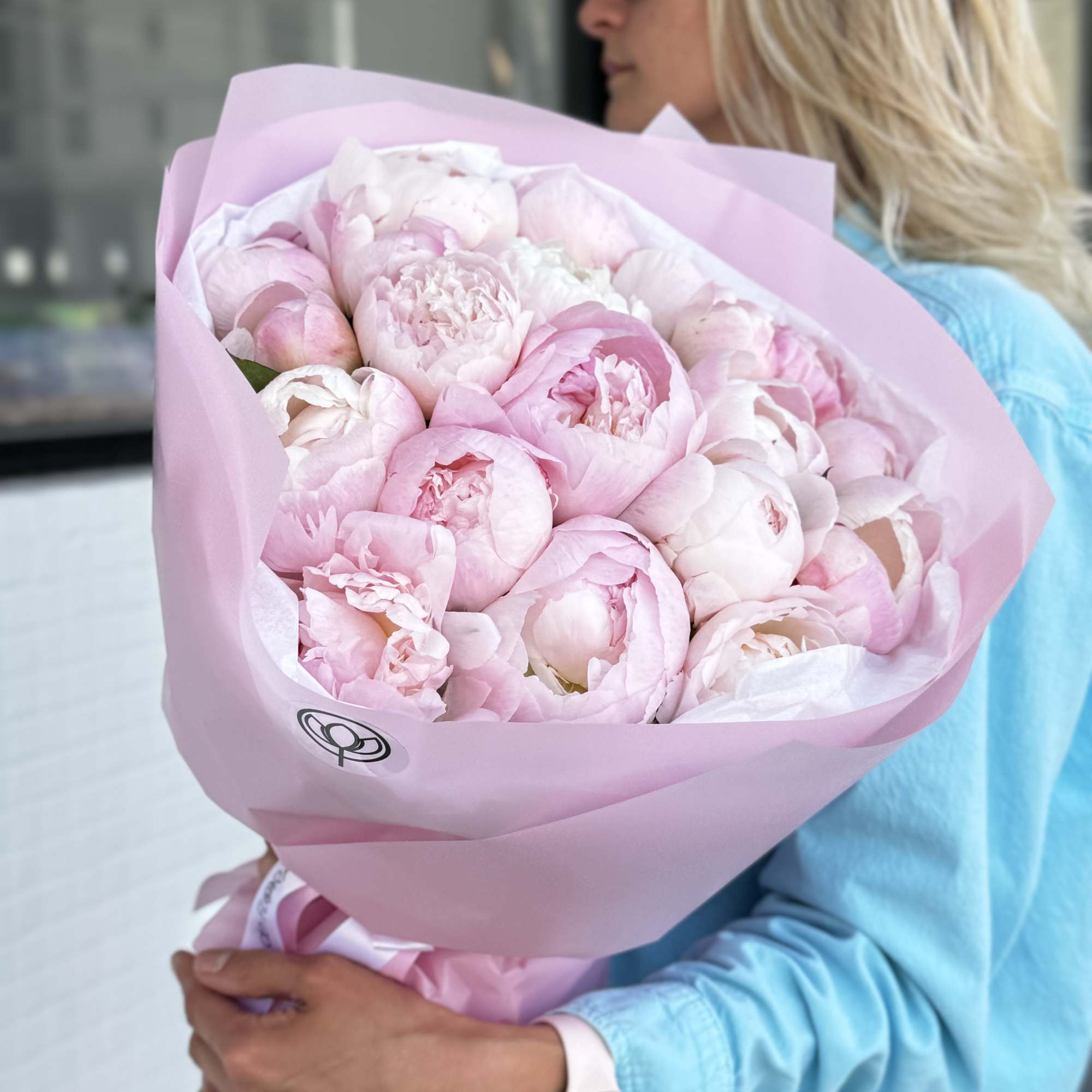 Woman holding a large bouquet of pale pink peonies wrapped in pink paper