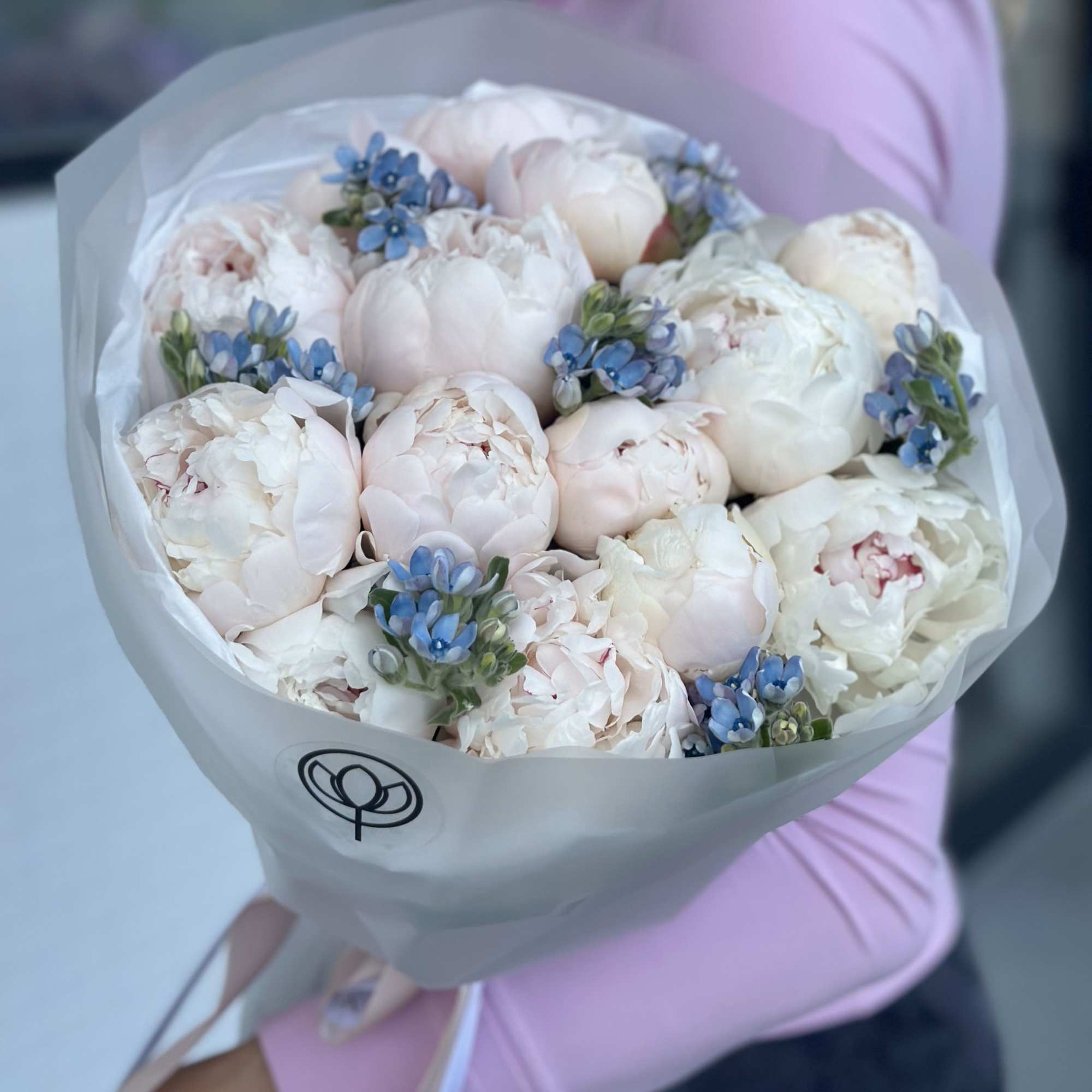 Bouquet of pale pink peonies with small blue flowers wrapped in white paper