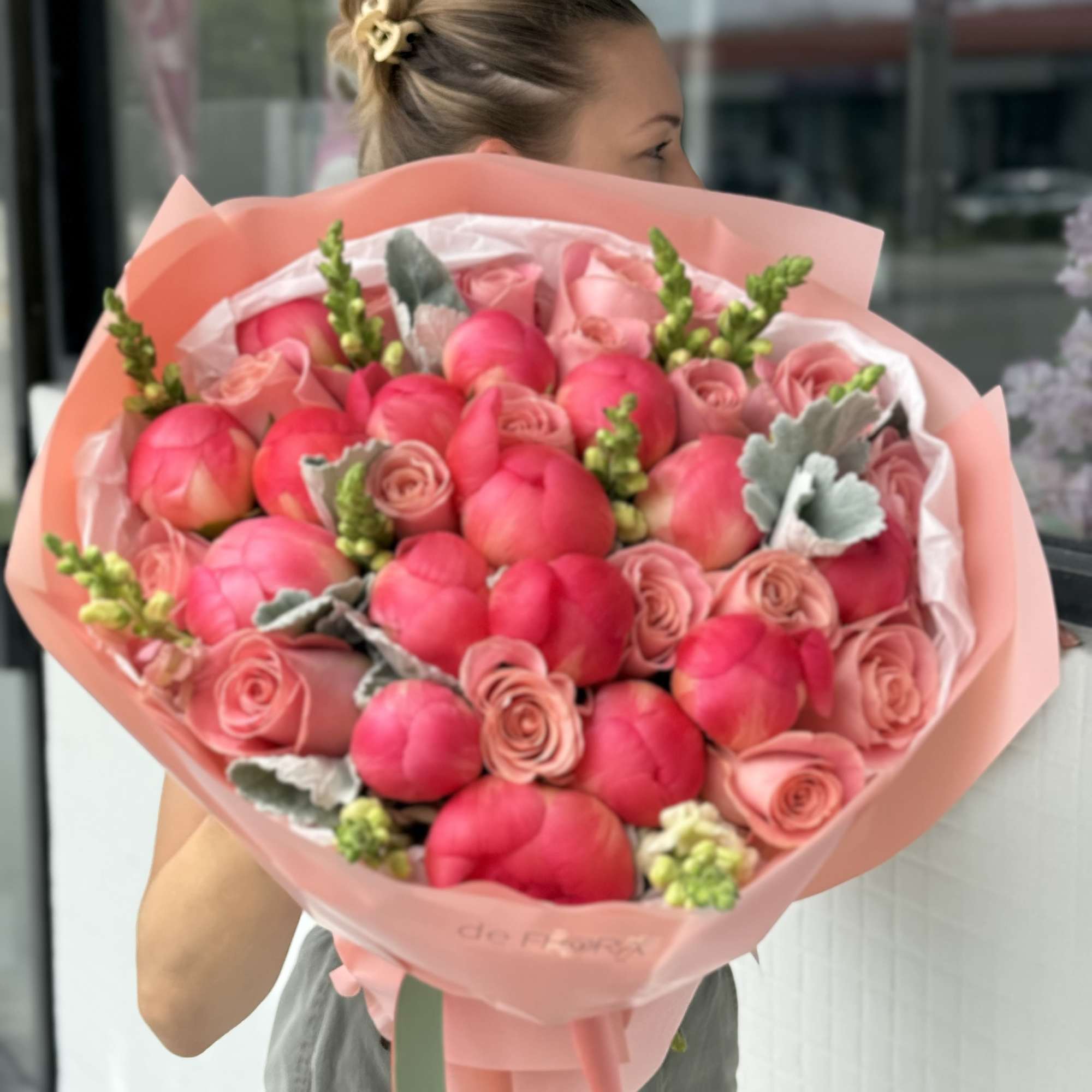 Large pink bouquet of roses and tulip-like blooms wrapped in peach paper