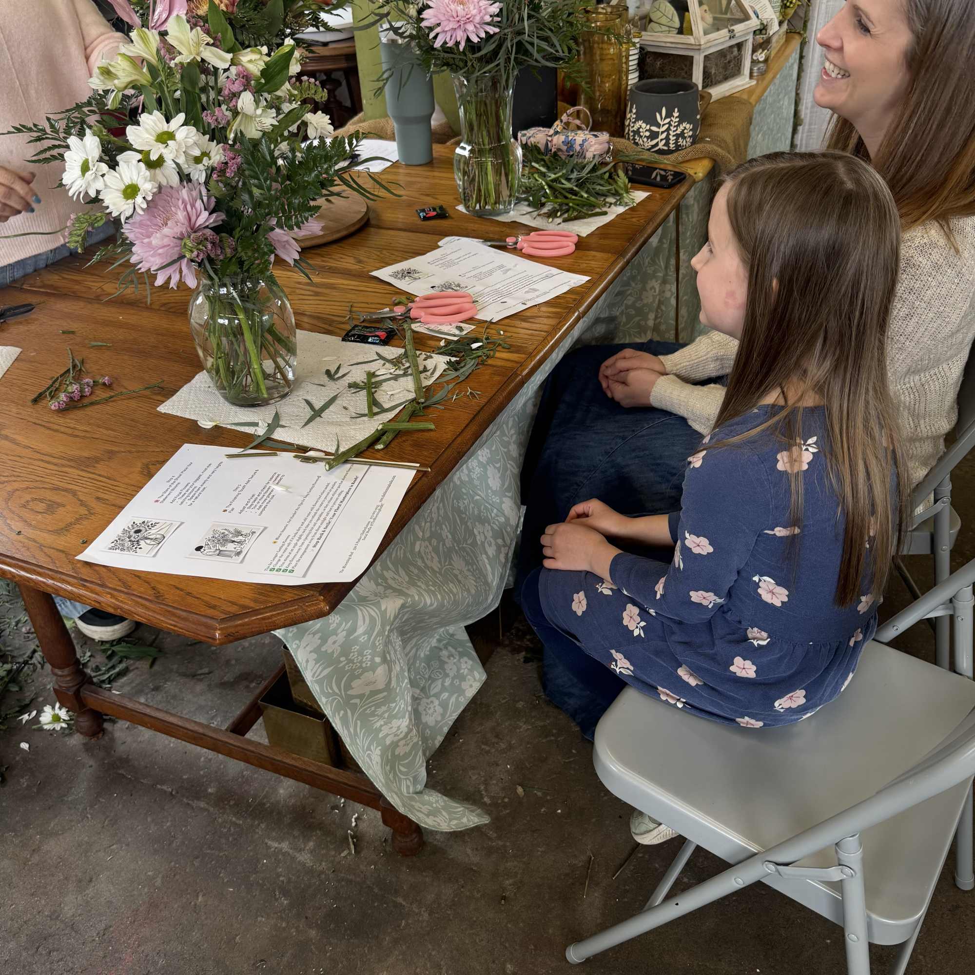 People arranging mixed flowers in glass vases at a table