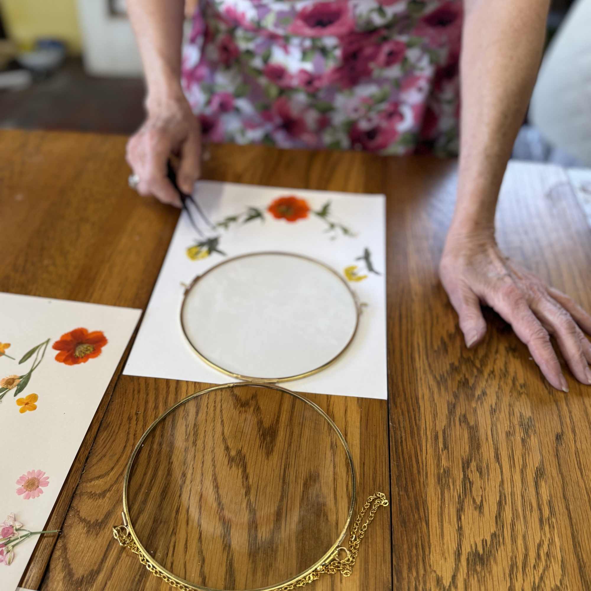 Person arranging floral prints and gold hoops on a wooden table
