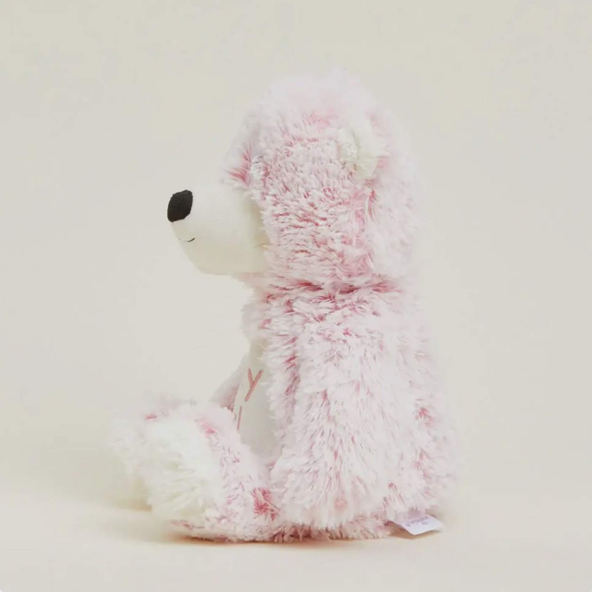 Pink and white plush teddy bear sitting in profile