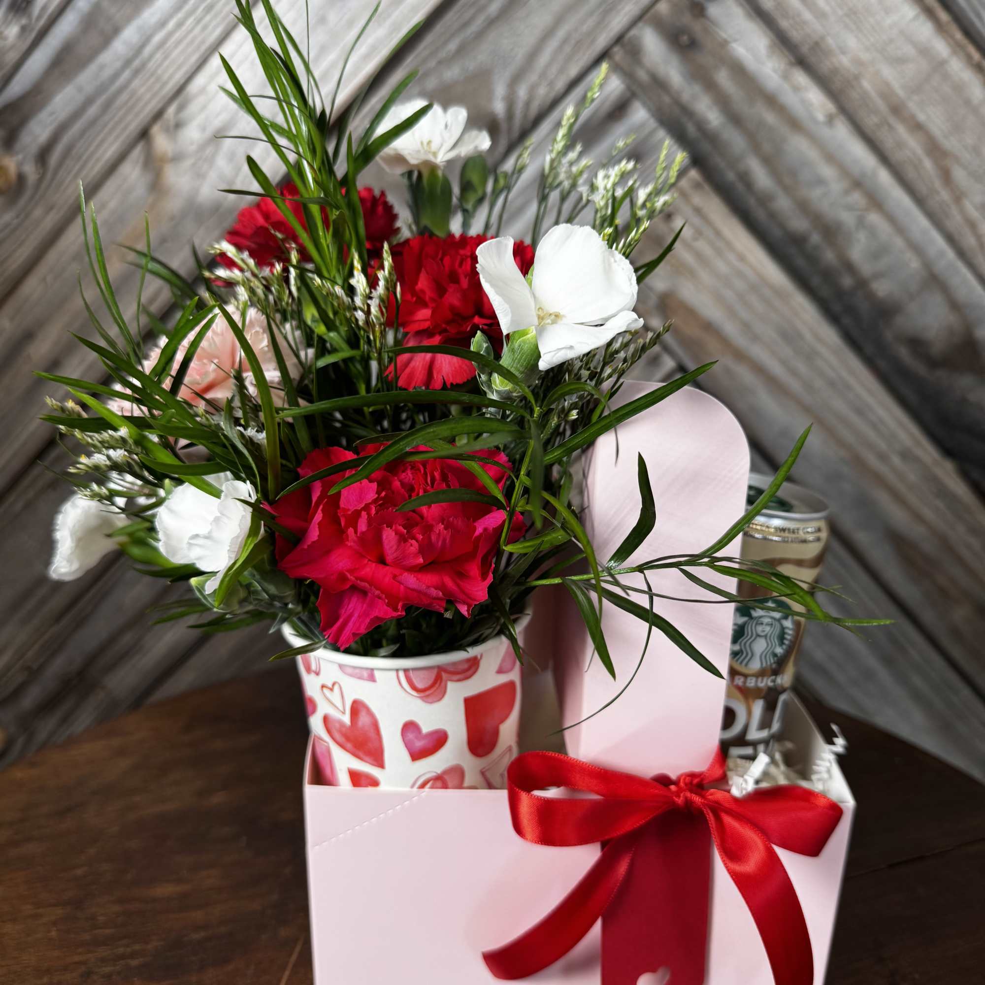 Red and white carnations in a heart-patterned cup with a gift box and ribbon