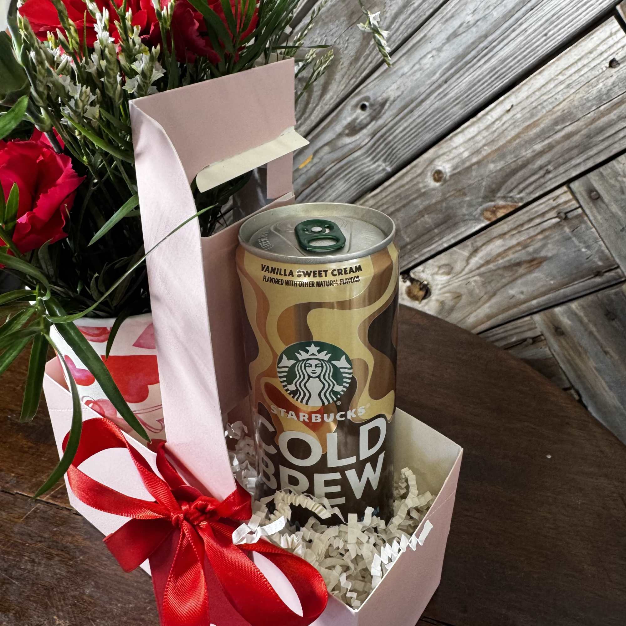 Gift box with a Starbucks cold brew can and red flowers tied with a ribbon