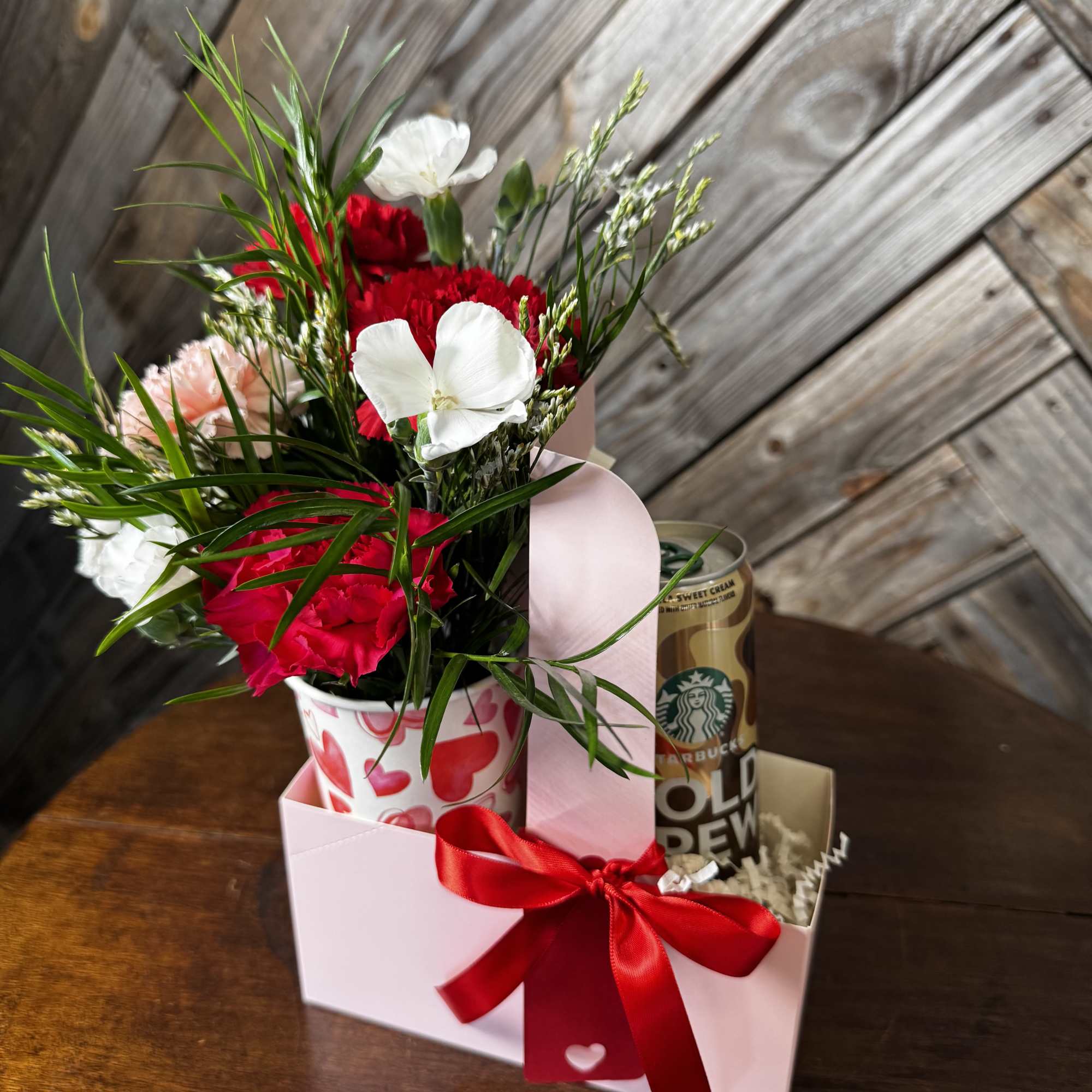 Bouquet of red and white carnations in a heart-patterned cup with a gift box