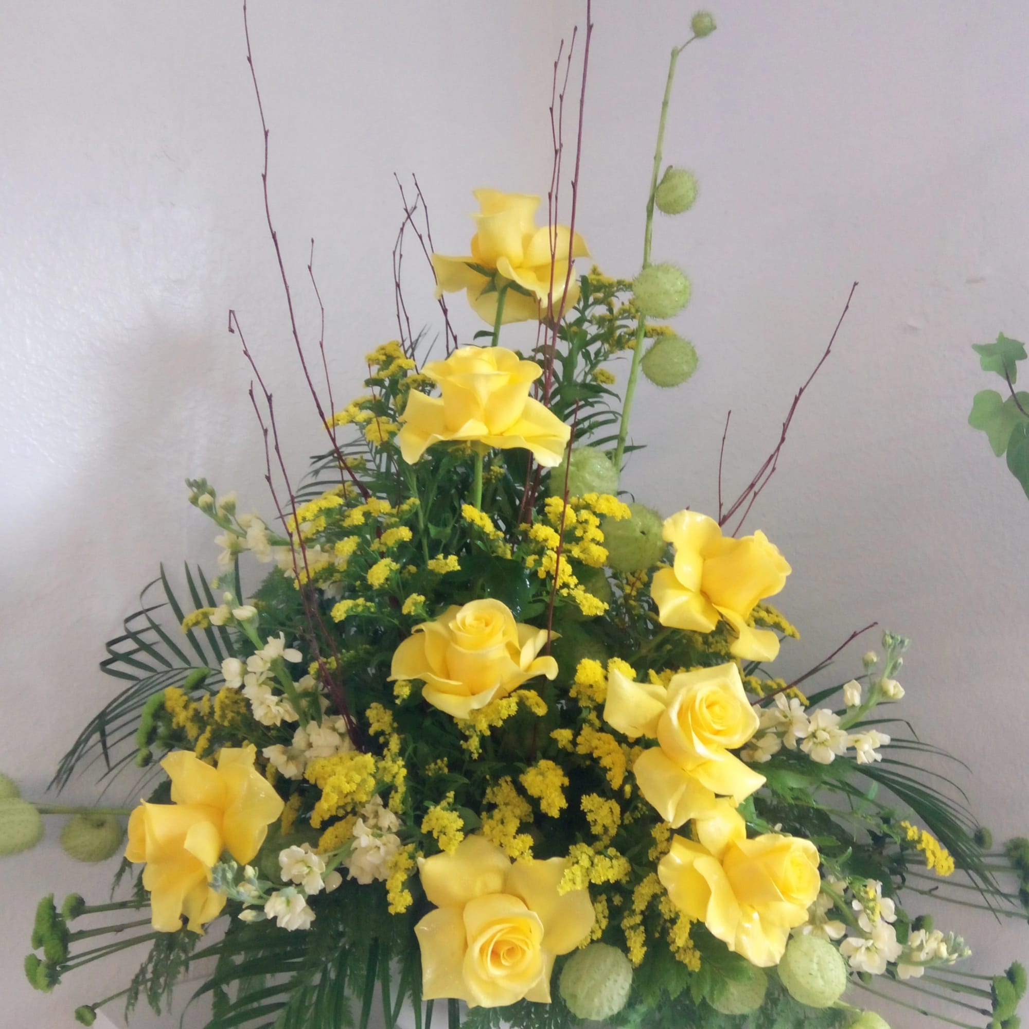 Tall arrangement of yellow roses with white flowers and green accents