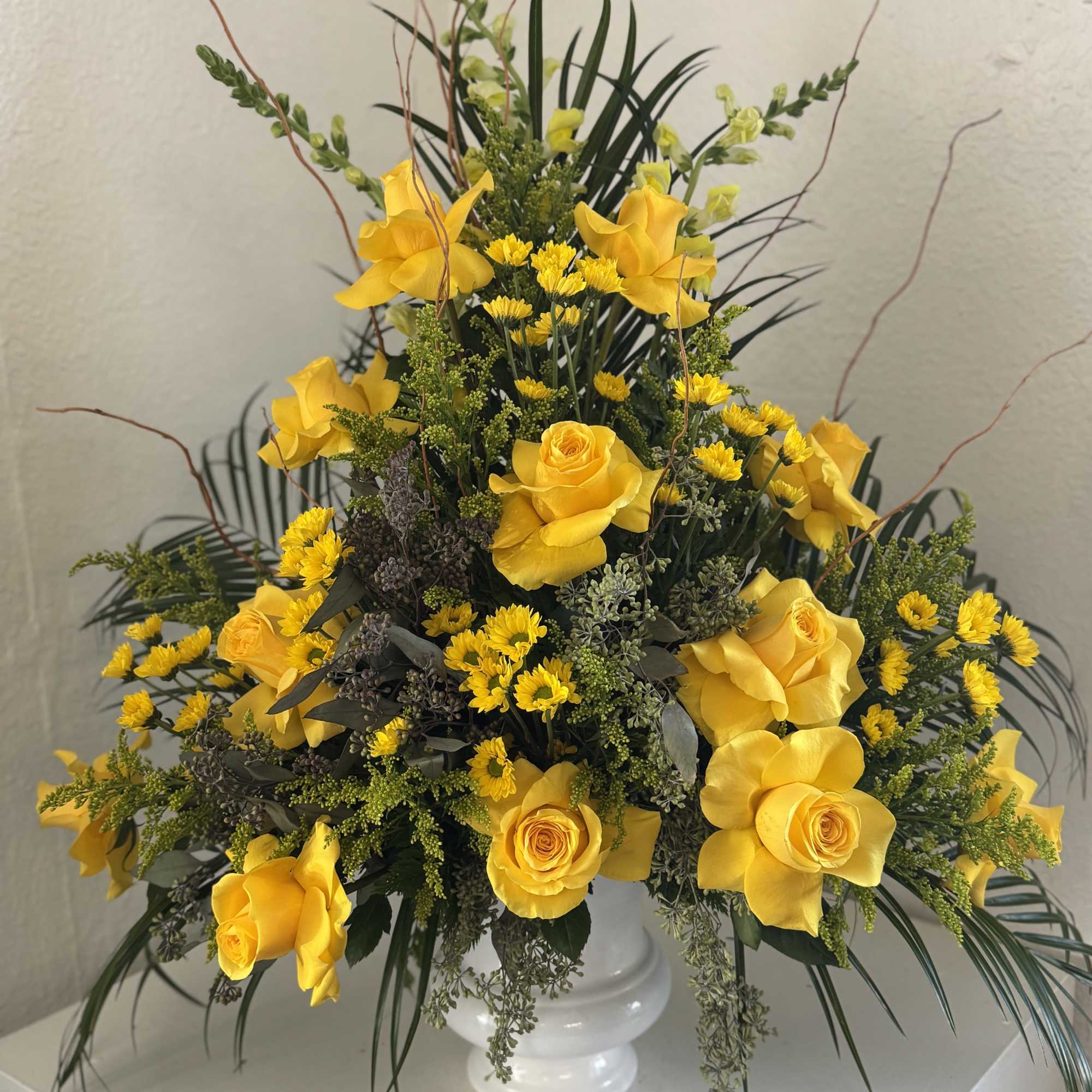 Yellow roses and small yellow daisies in a white pedestal vase