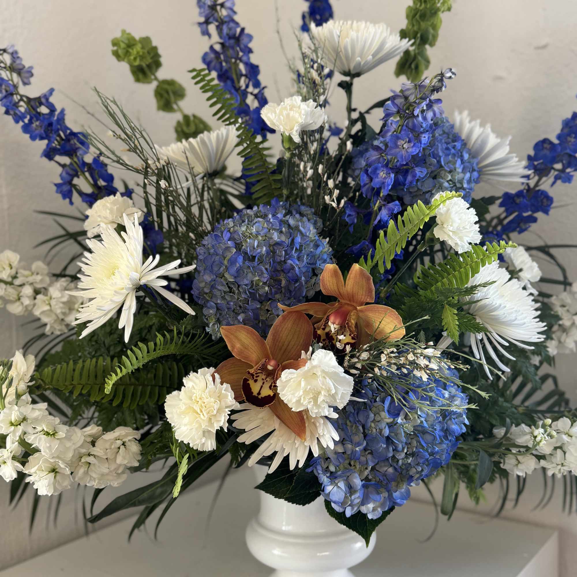 Blue and white floral arrangement in a white vase with orange orchids