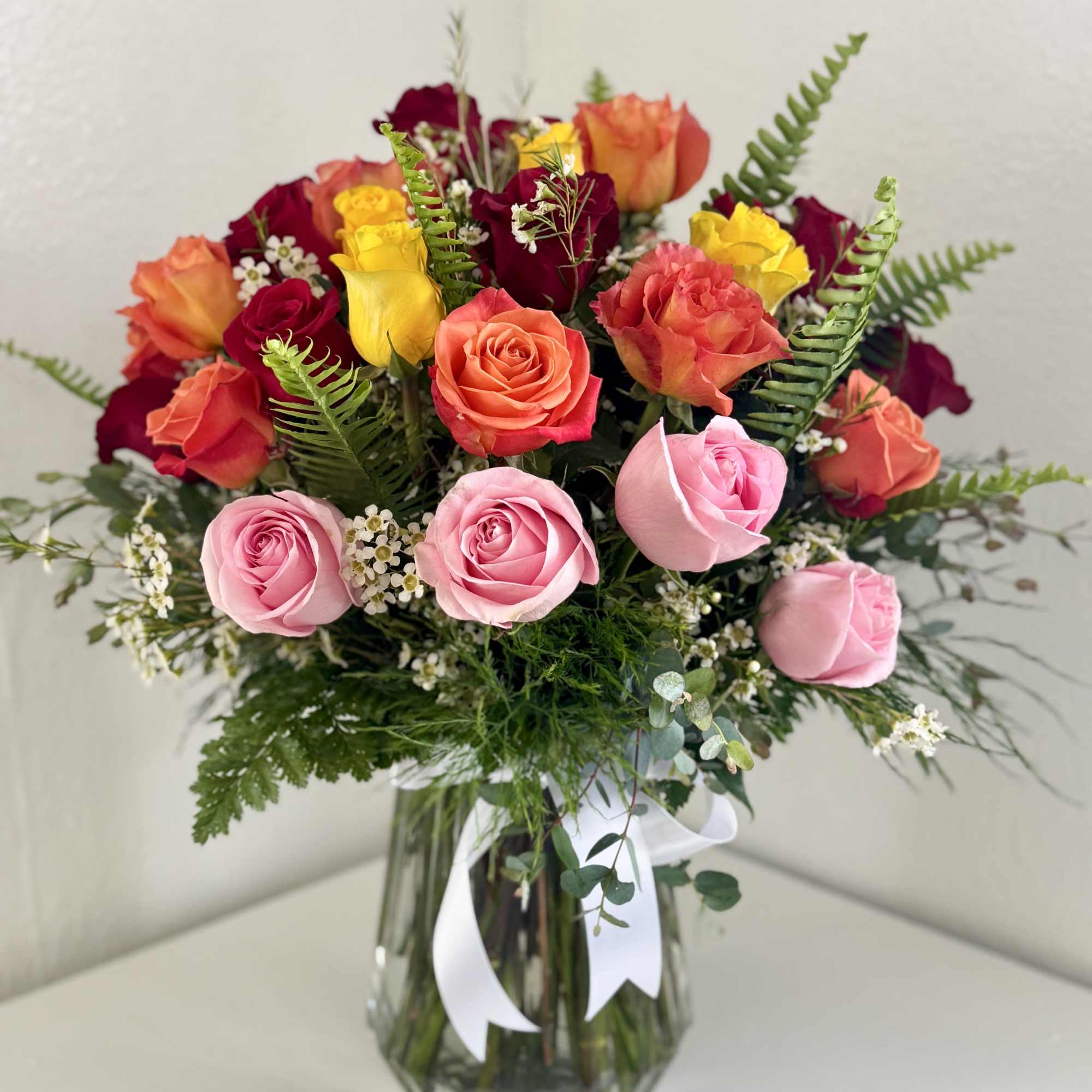 Mixed roses in pink, coral, yellow, and burgundy in a glass vase