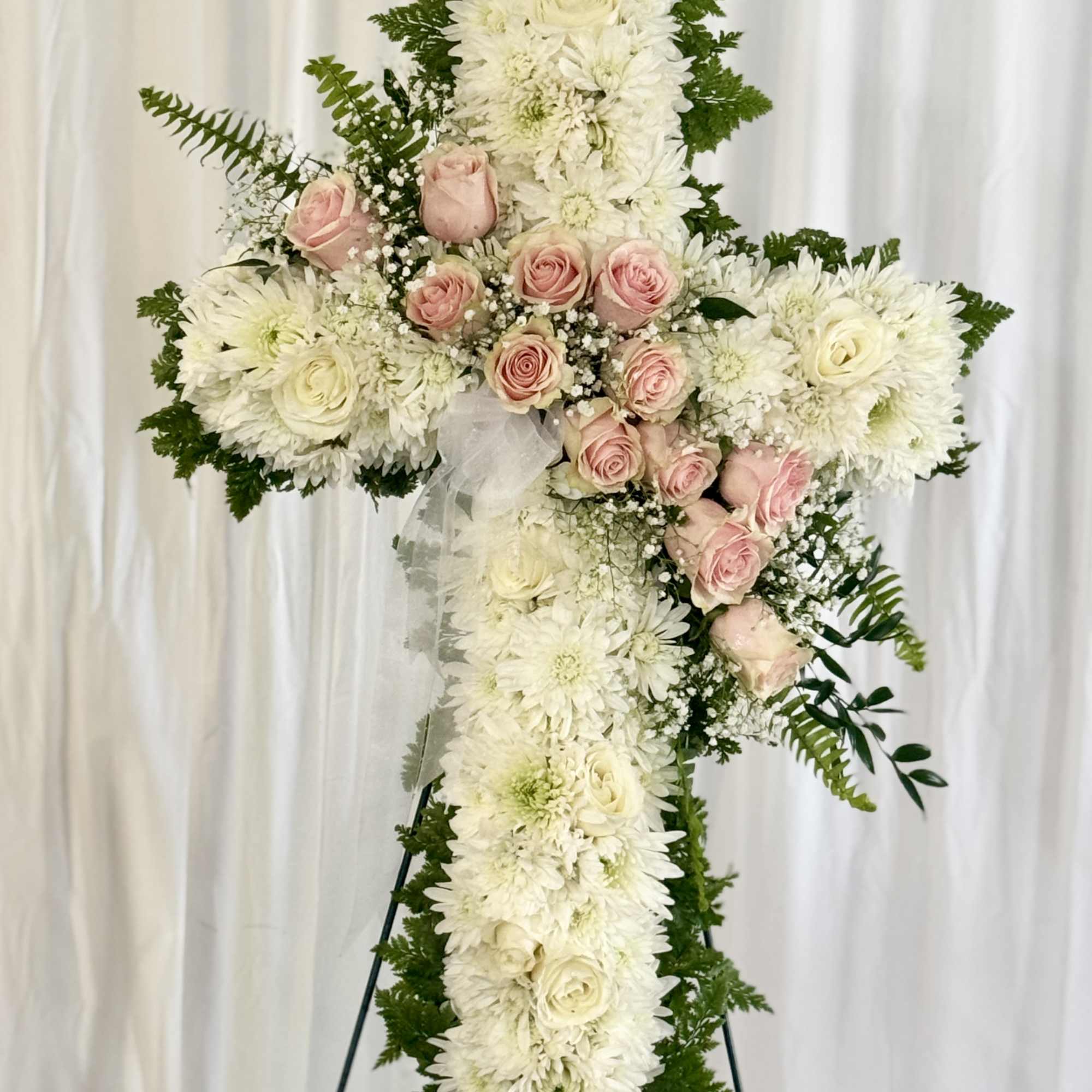 White floral cross with pink roses on a stand
