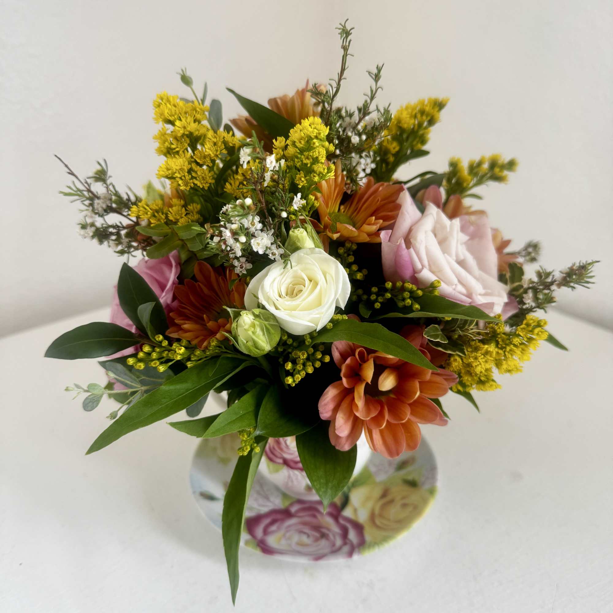 Mixed bouquet with white and pink roses, orange blooms, and yellow filler flowers in a floral vase