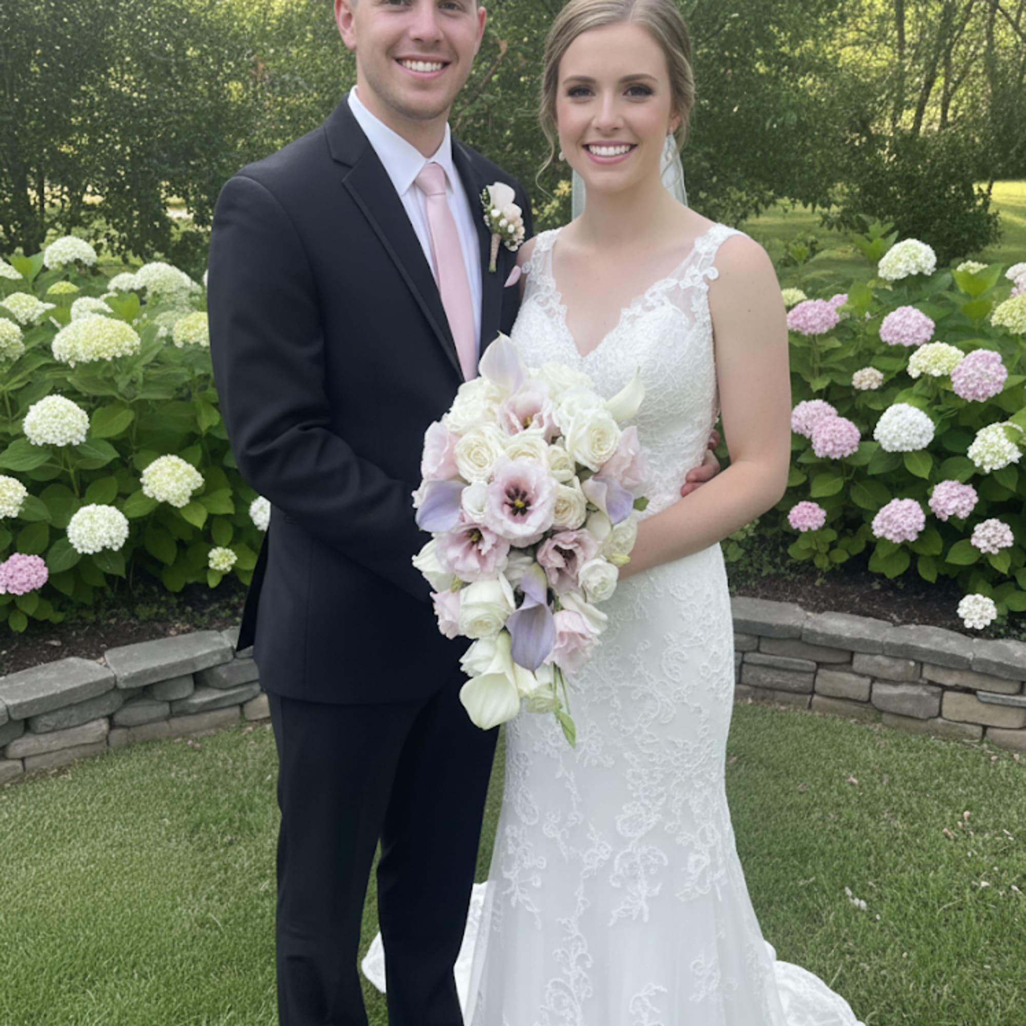Bride and groom posing with a white and blush wedding bouquet outdoors