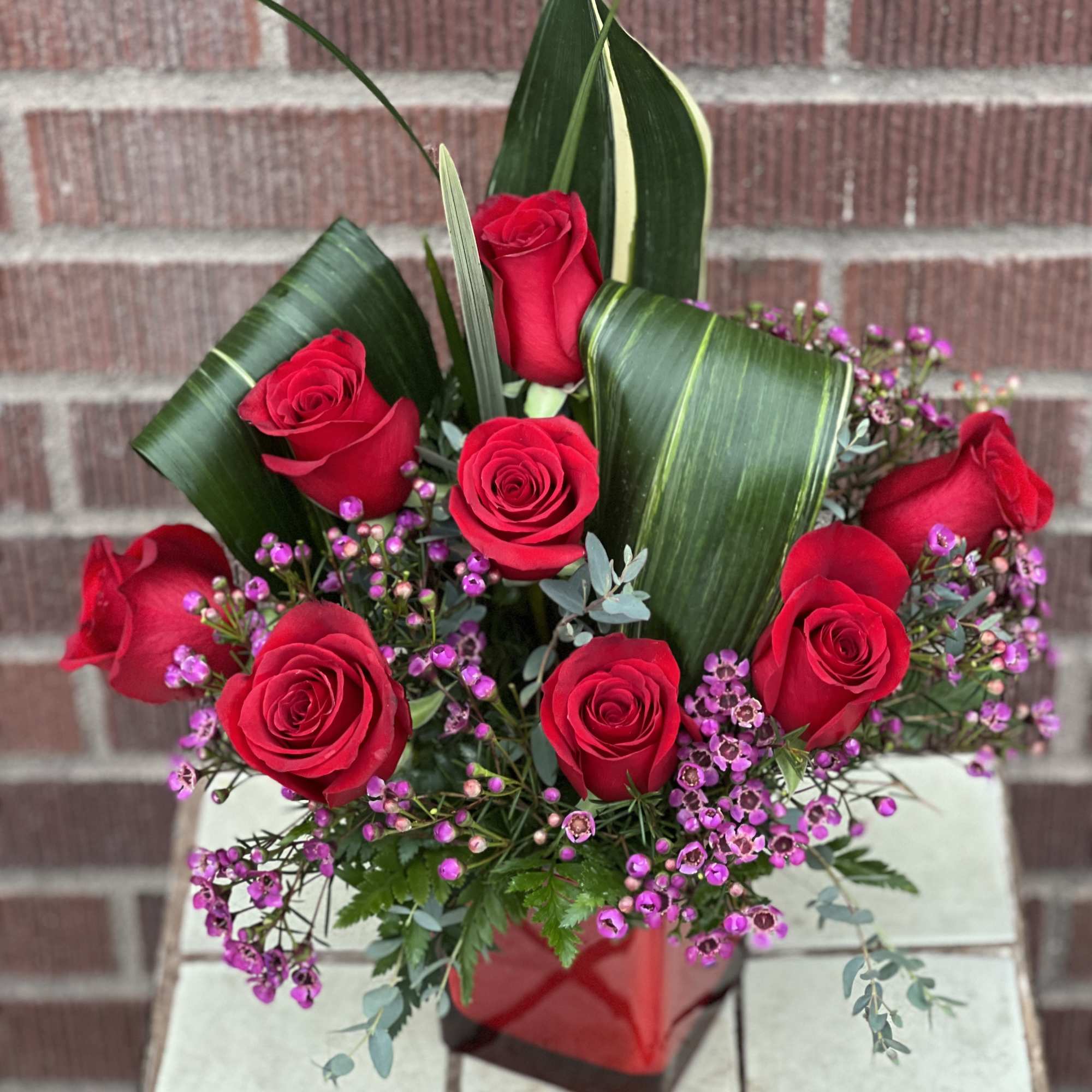 Red roses arranged with purple filler in a red vase
