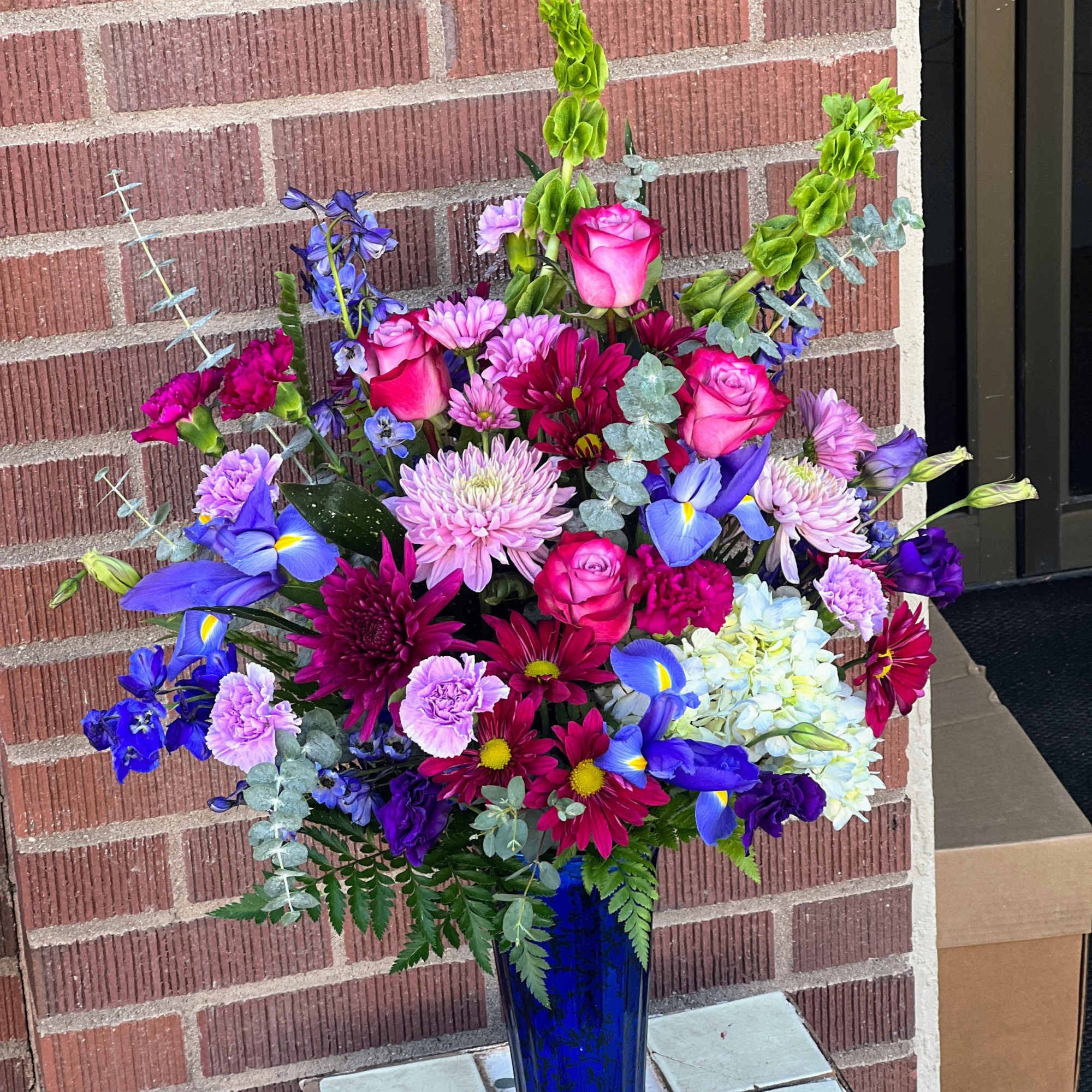 Tall mixed bouquet in a blue glass vase with pink, purple, and blue flowers