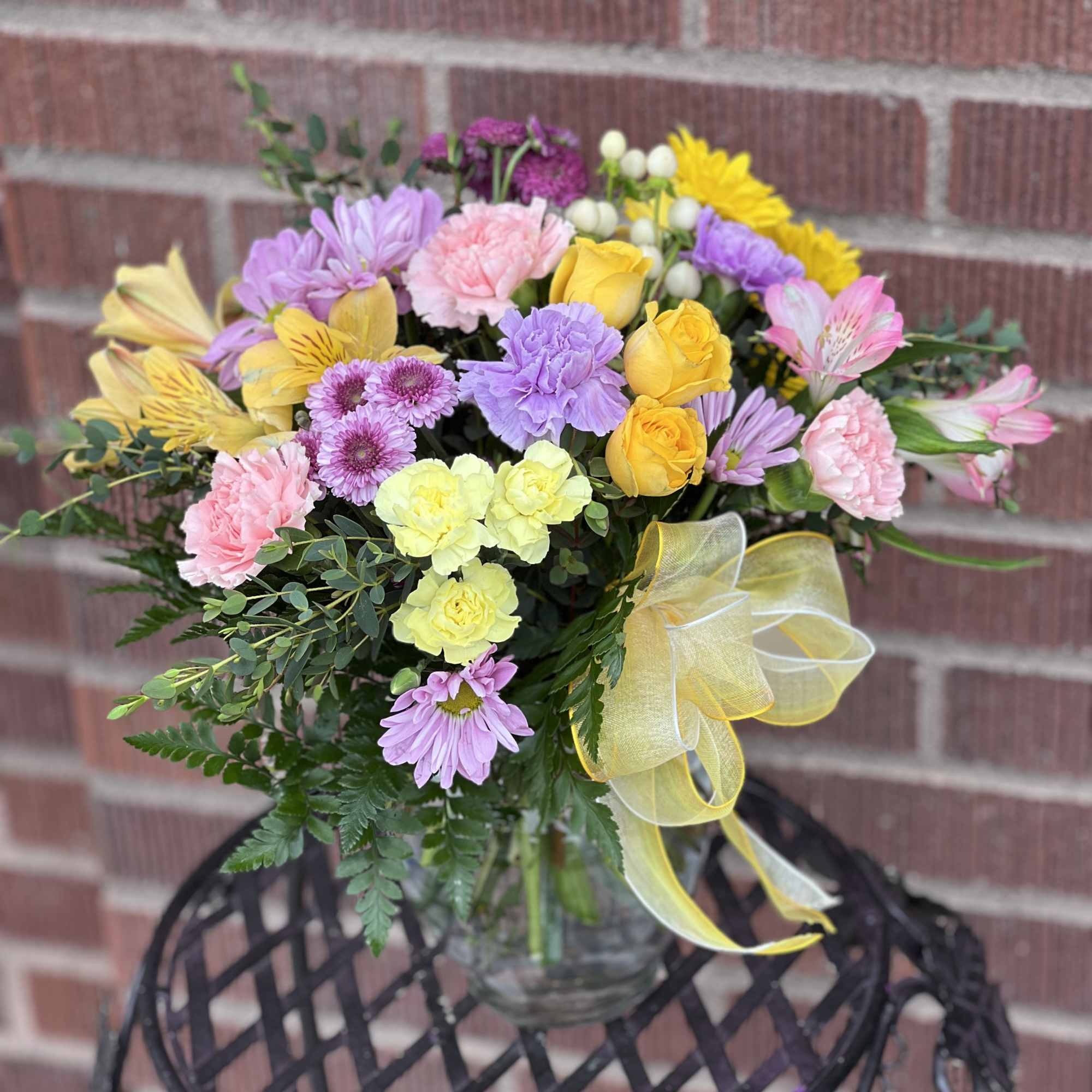 Mixed pastel bouquet in a clear glass vase with a yellow ribbon