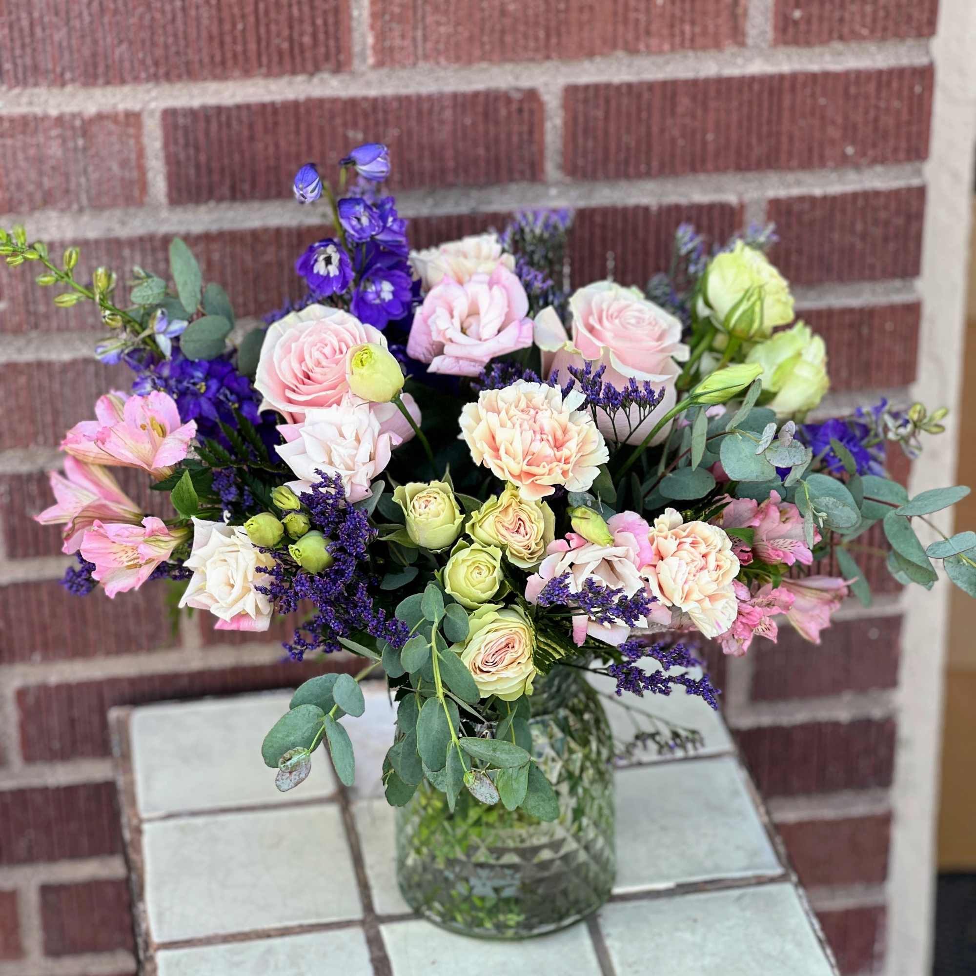 Pink and cream roses with purple flowers in a glass vase
